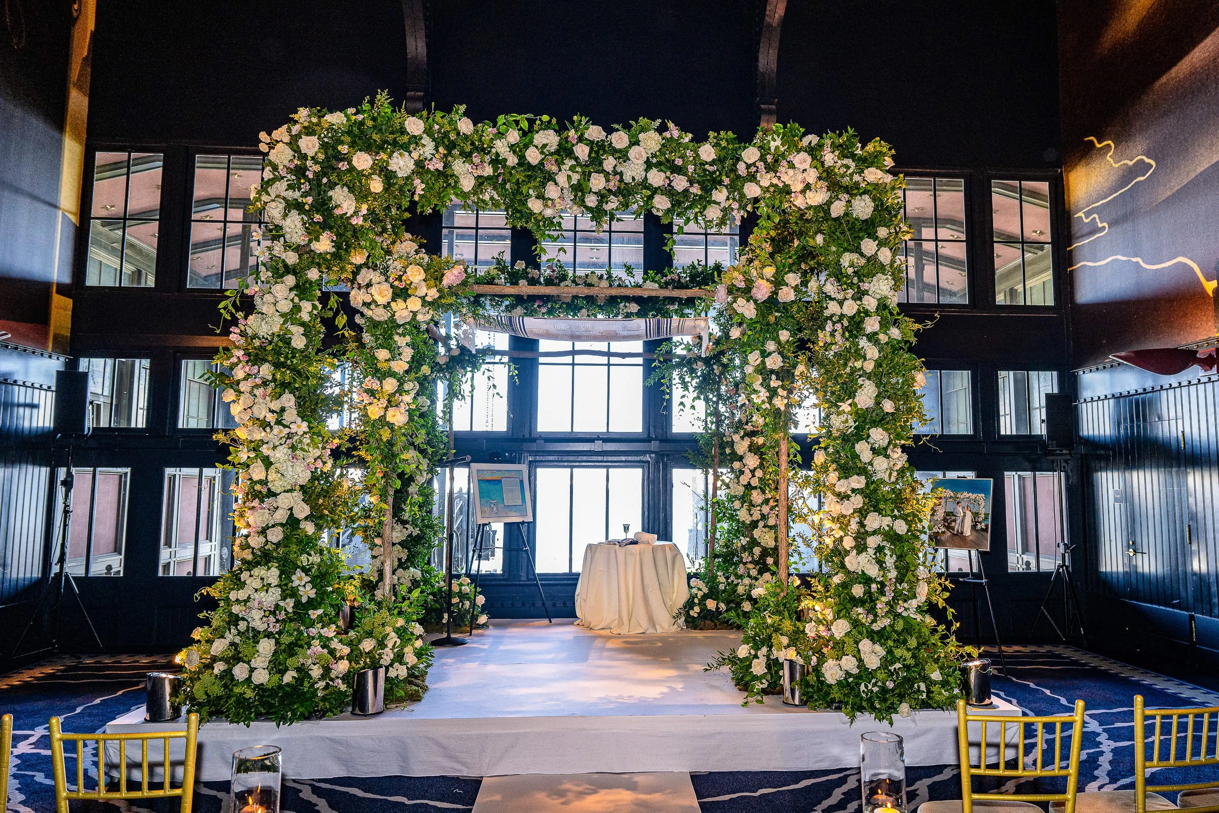 The chuppah of white roses and greenery against the harbour windows — Casa Cipriani, New York