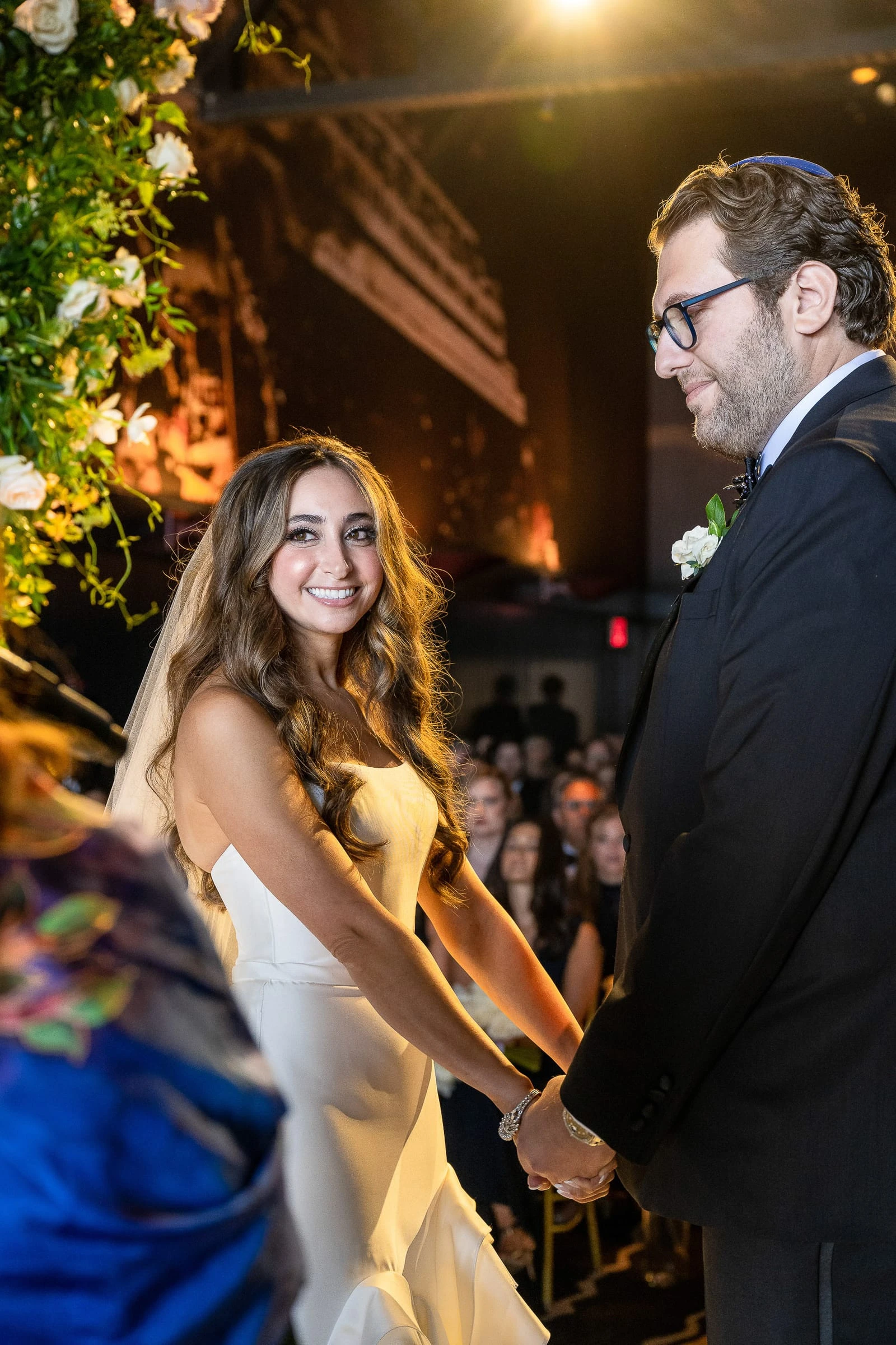 The bride glancing back as the couple hold hands beneath the chuppah — Casa Cipriani, New York