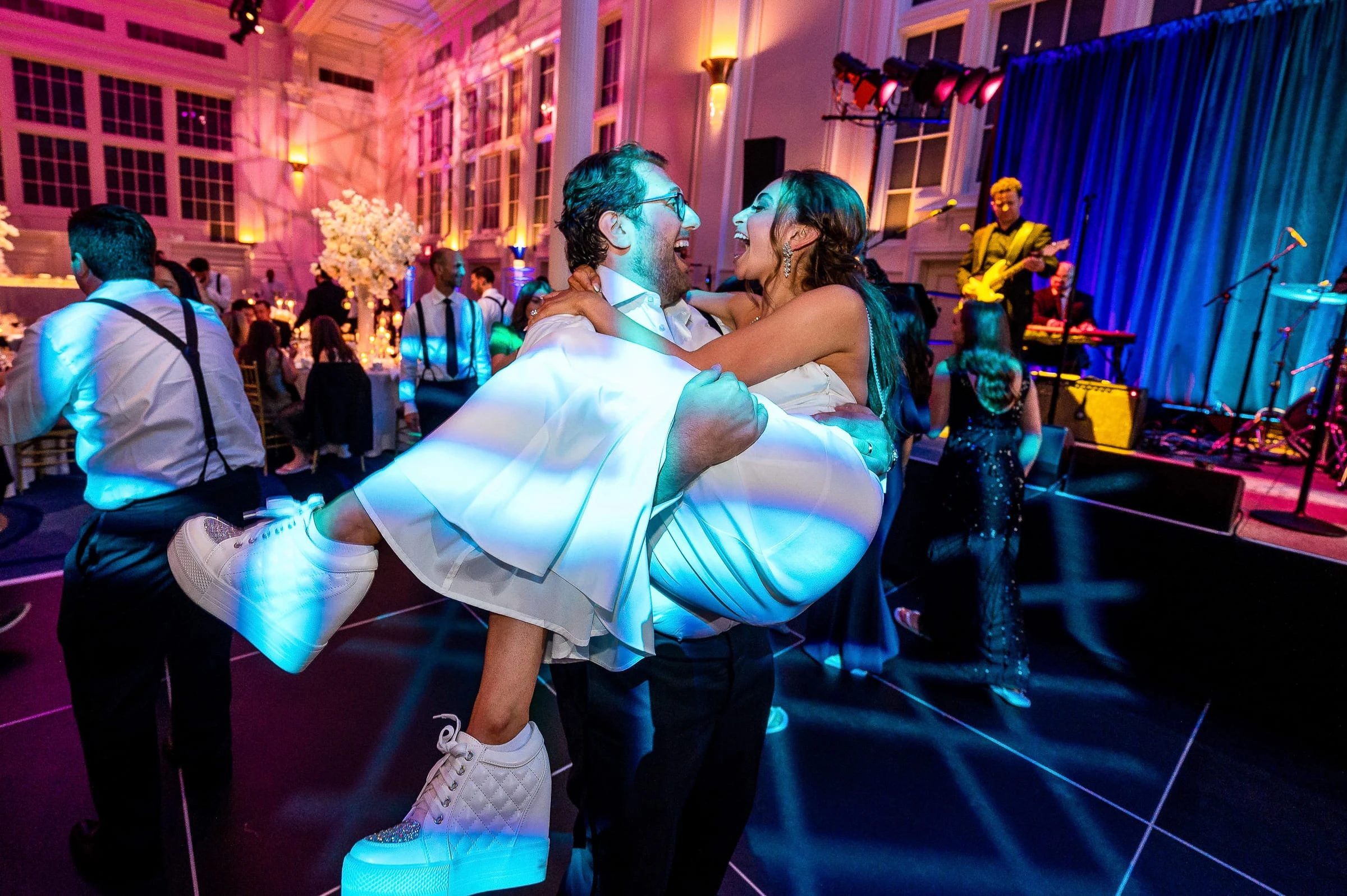 The groom carrying the bride across the dance floor in pink and blue stage light — Casa Cipriani, New York