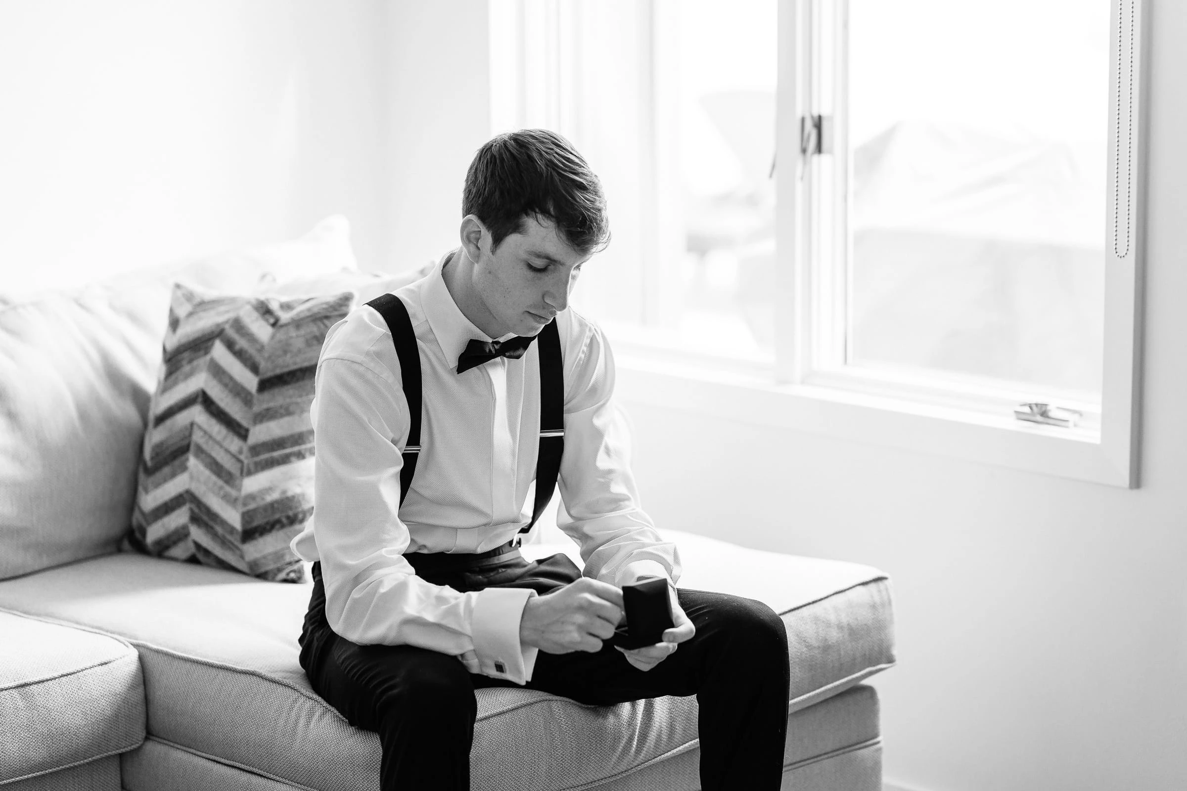 The groom waiting alone on the sofa in his braces, in black and white — Shadowbrook at Shrewsbury, Shrewsbury