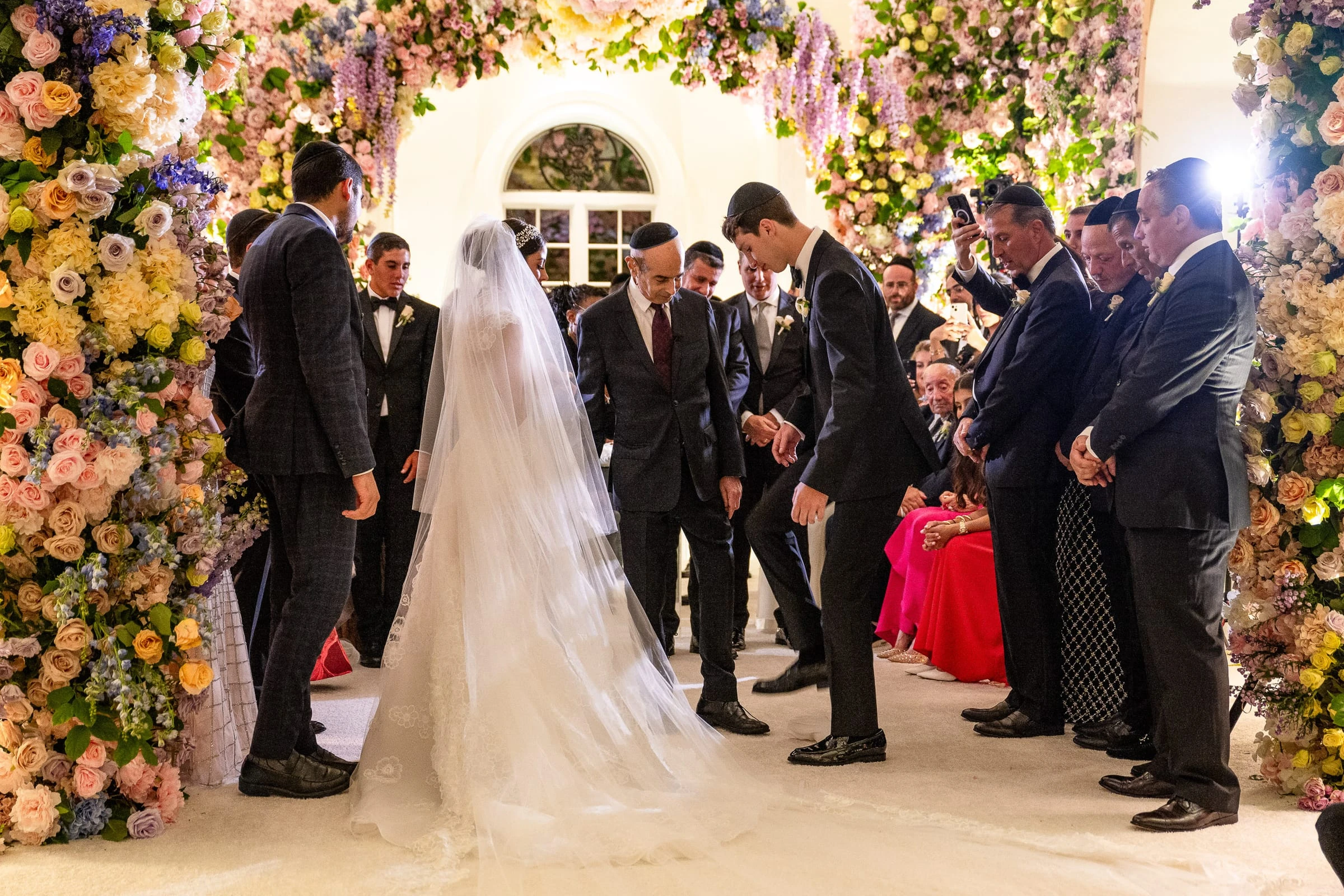The bride beneath her long veil facing the groom under the flowered chuppah — Shadowbrook at Shrewsbury, Shrewsbury