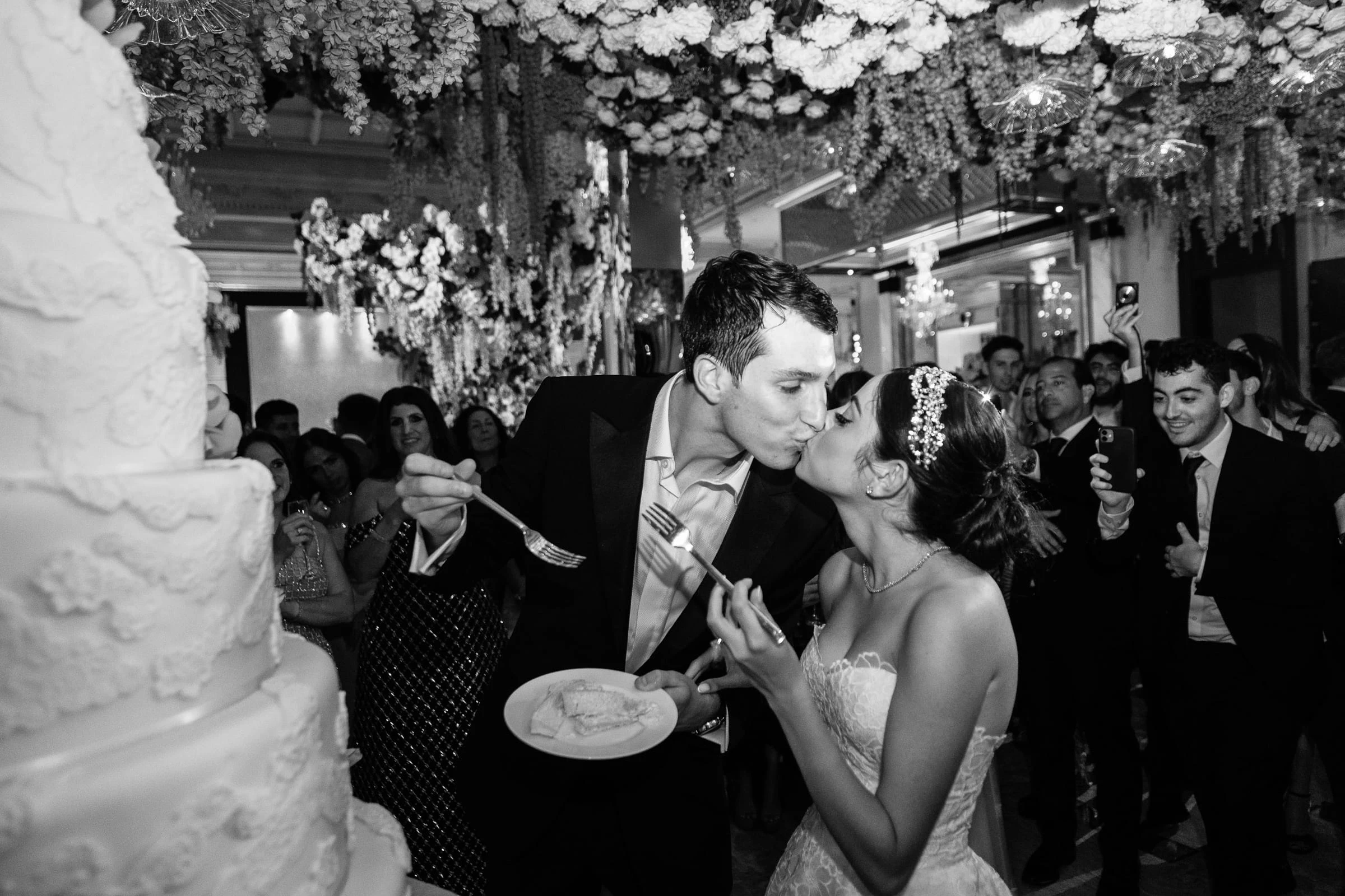 The bride and groom feeding each other cake as guests look on, in black and white — Shadowbrook at Shrewsbury, Shrewsbury