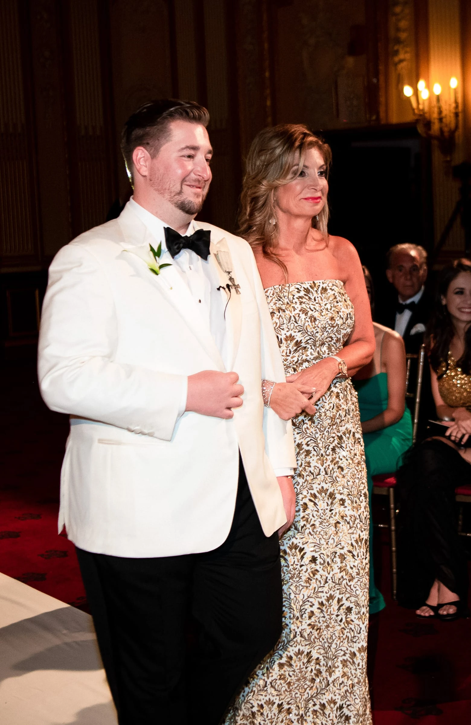 The other groom entering the aisle arm in arm with a woman in gold — Metropolitan Club, New York