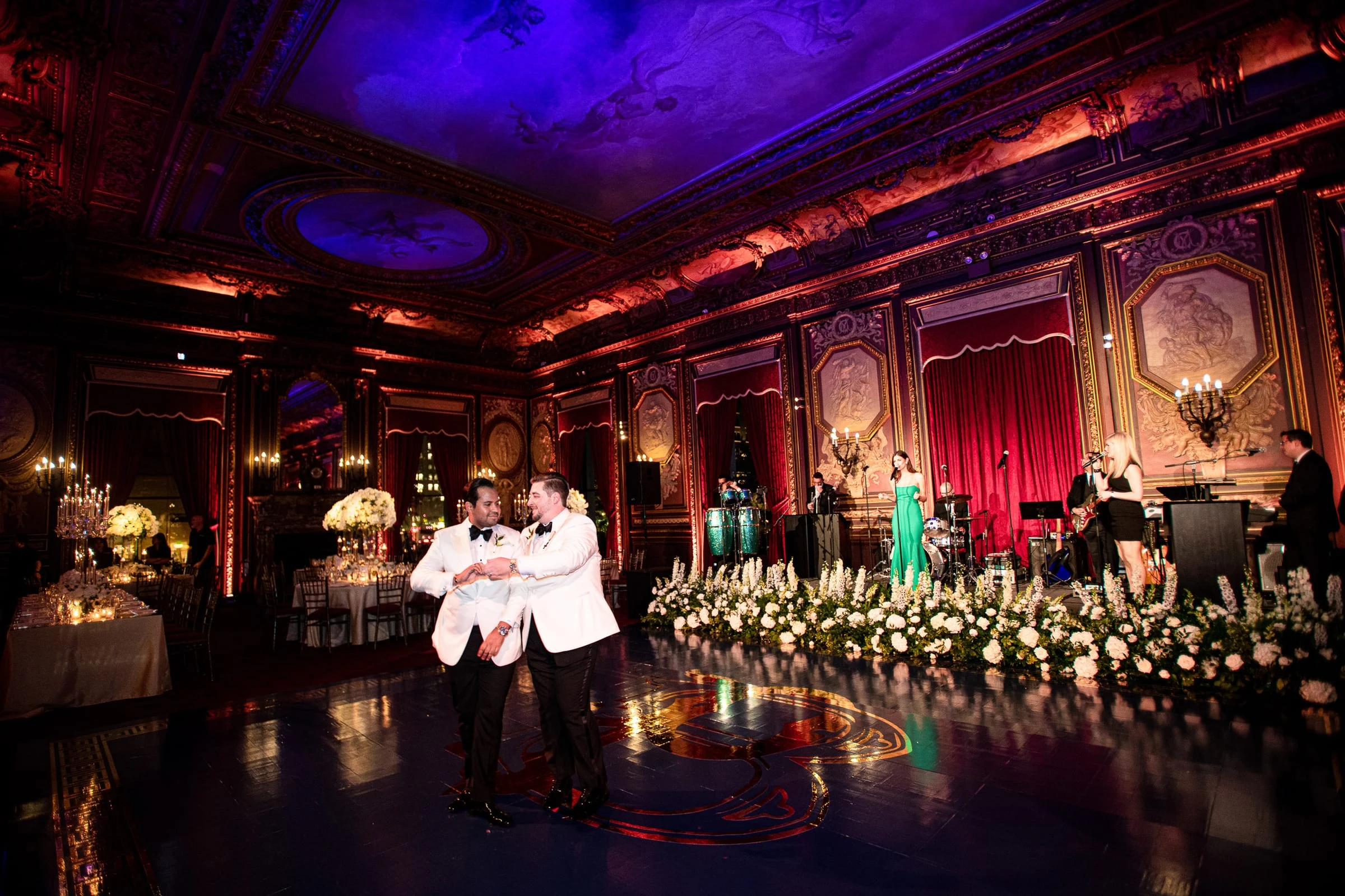 The two grooms in white jackets dancing on the floor beside a long bank of white flowers — Metropolitan Club, New York