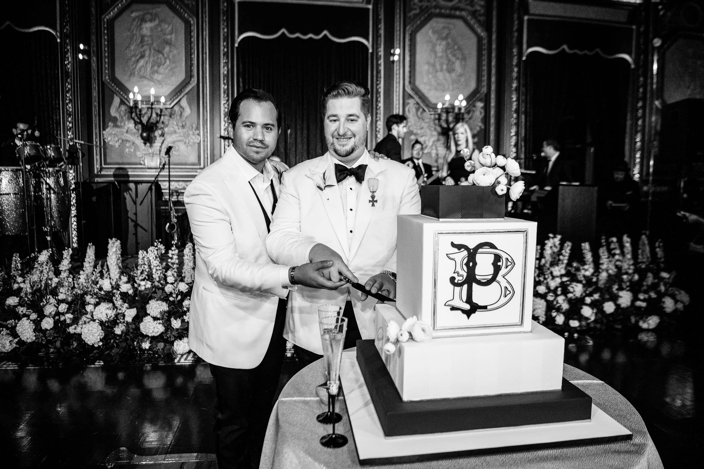 The two grooms cutting a monogrammed cake together, in black and white — Metropolitan Club, New York