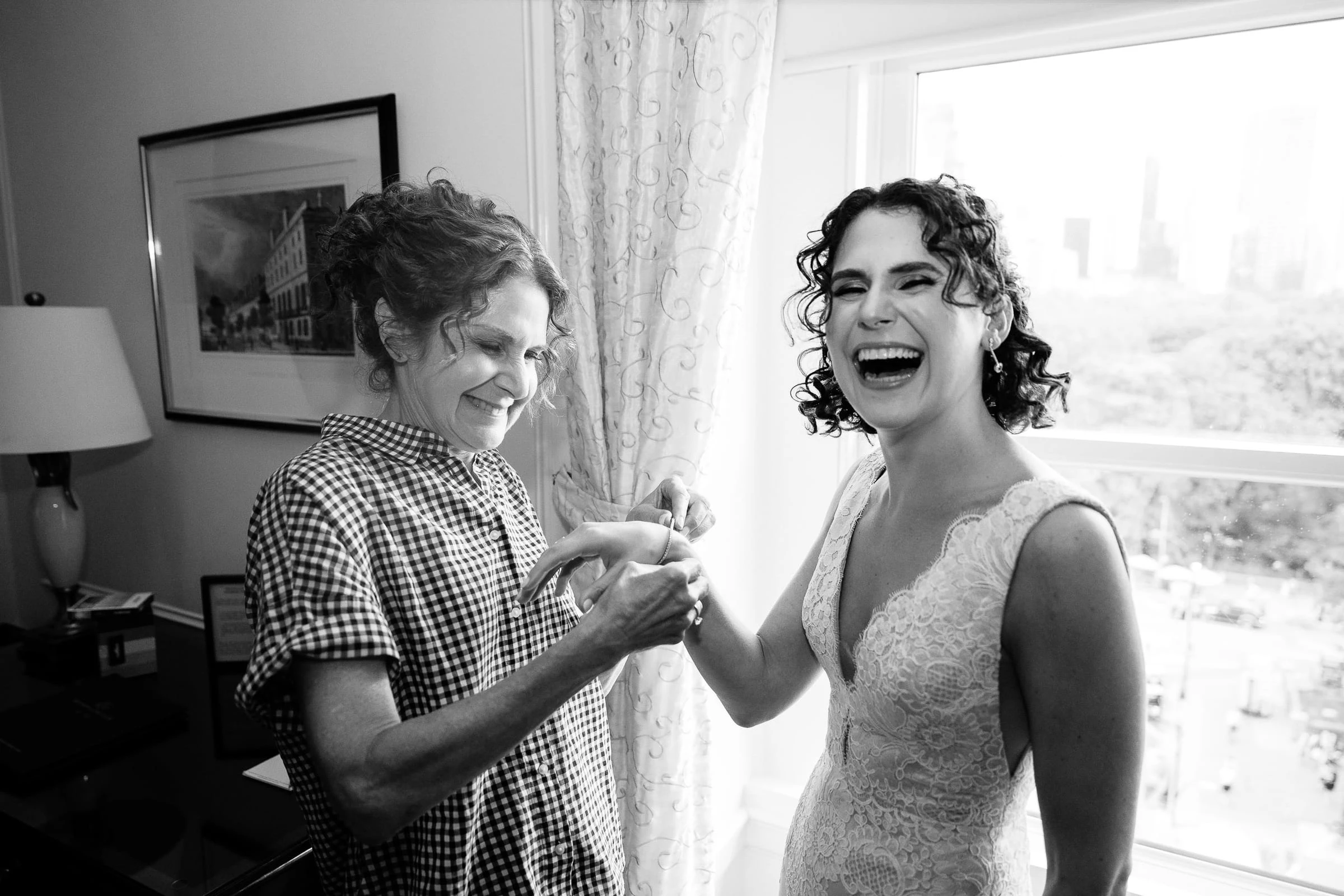 The bride laughing as a woman takes both her hands beside the window, in black and white — Metropolitan Club, New York