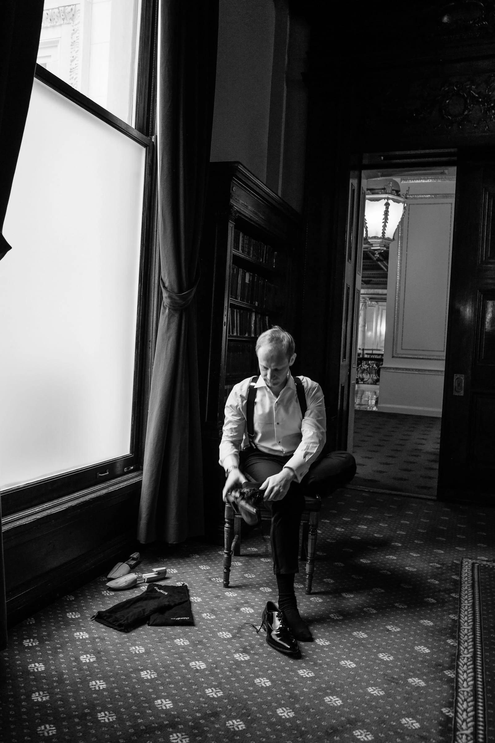 The groom sitting alone by a bright window before the ceremony, in black and white — Metropolitan Club, New York