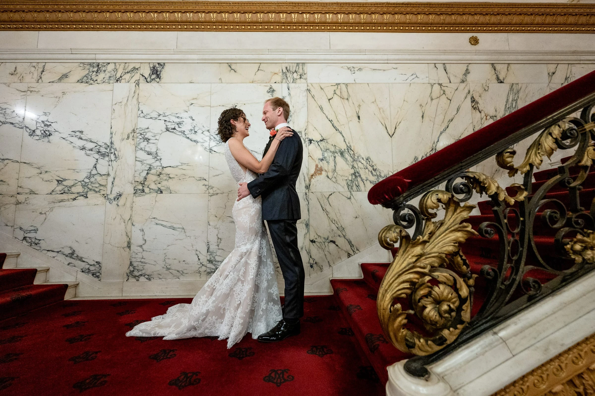 The couple together on the red-carpeted marble stairs beside the gilded banister — Metropolitan Club, New York