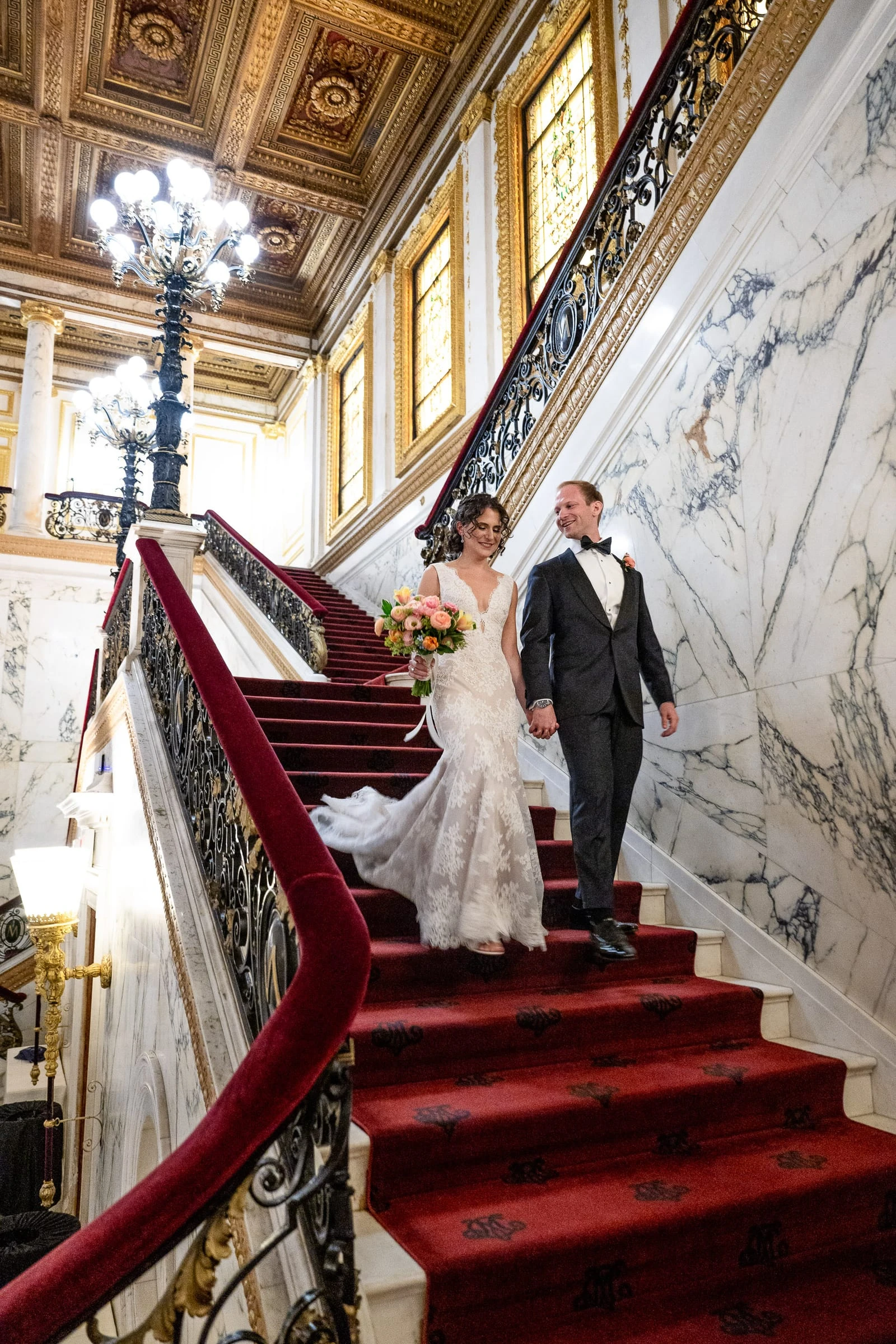 The bride and groom coming down the staircase, her bouquet in hand — Metropolitan Club, New York