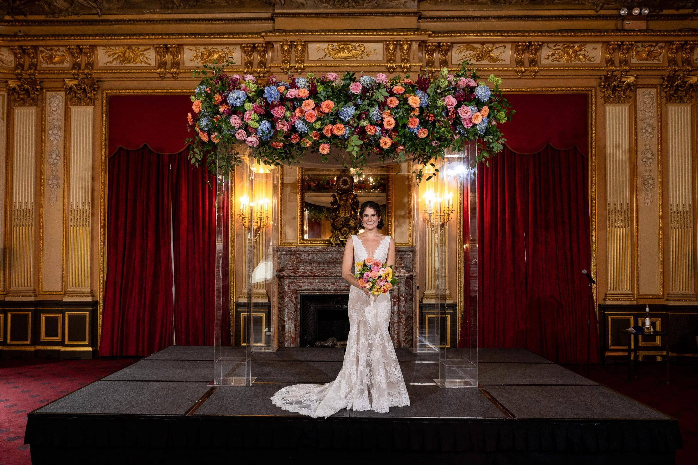 The bride alone on the ceremony platform beneath the flowered chuppah — Metropolitan Club, New York