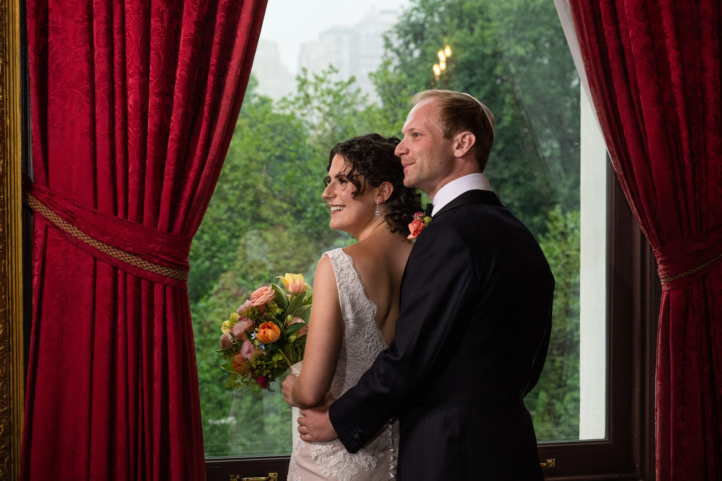 The couple at the window between red curtains, looking out to the park — Metropolitan Club, New York