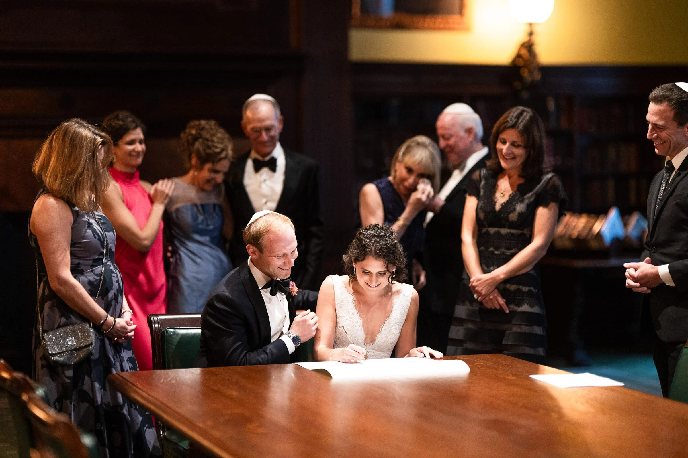 The couple signing at the long library table with family gathered around — Metropolitan Club, New York