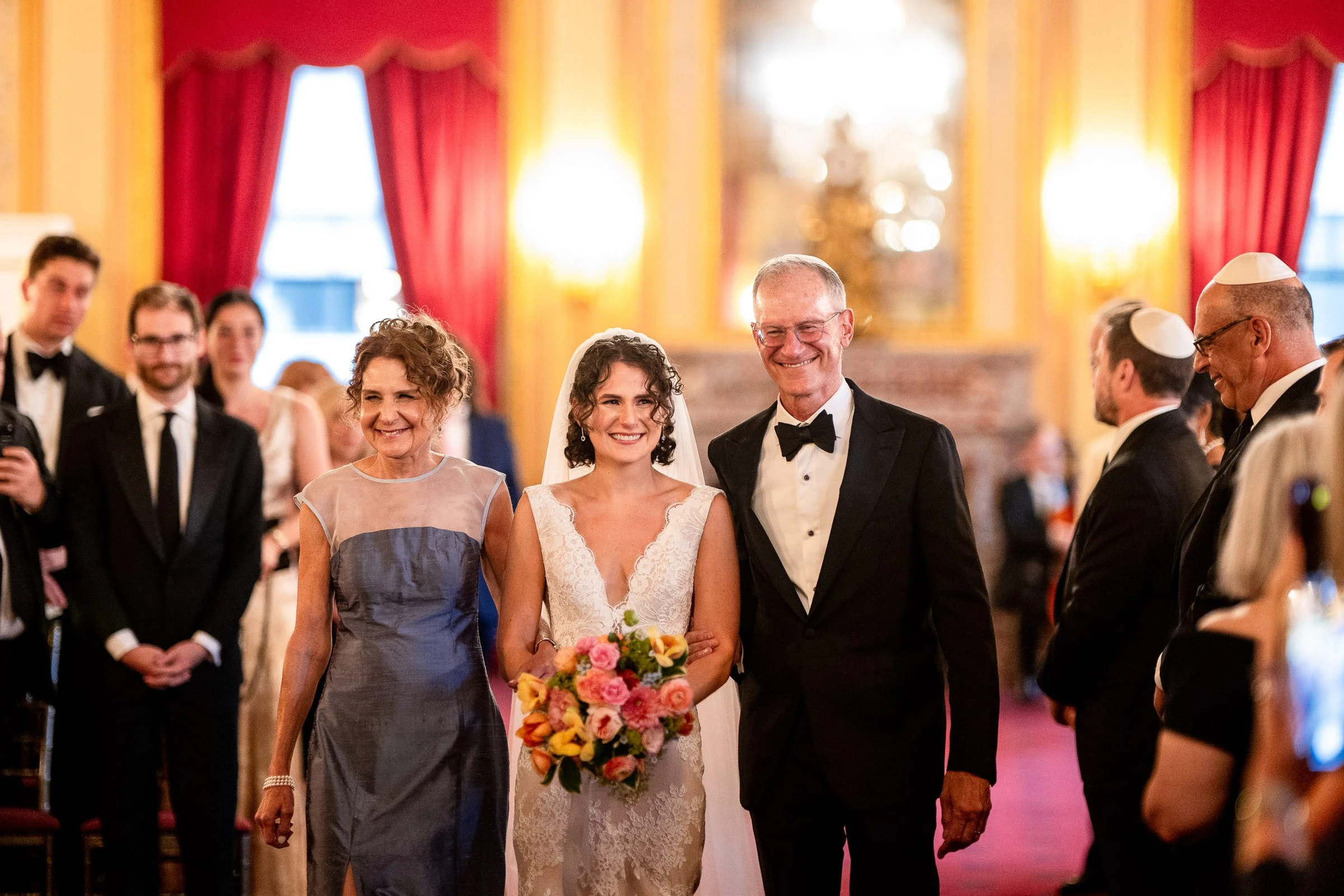 The bride walking the aisle between her parents, her bouquet in both hands — Metropolitan Club, New York