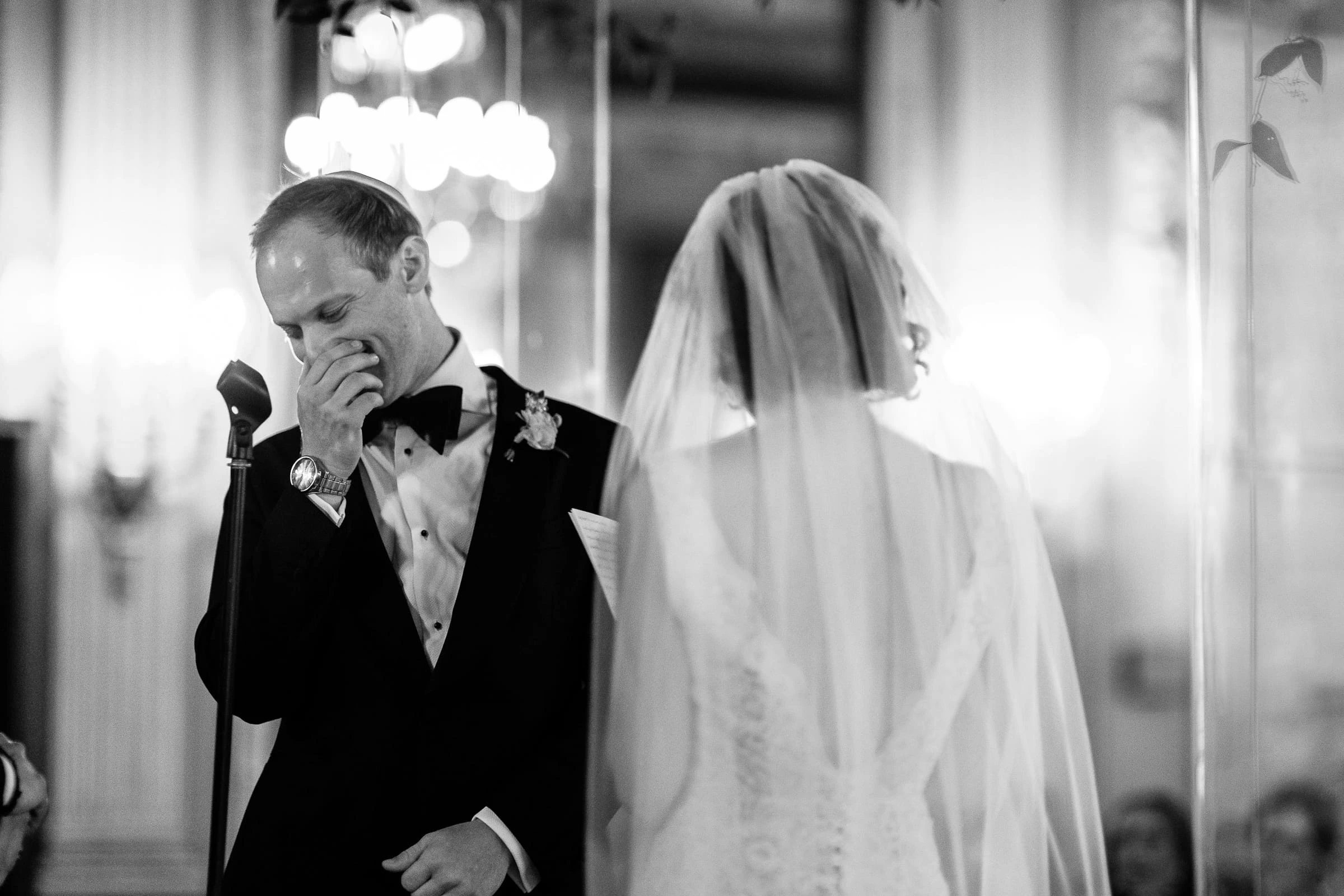 The groom wiping his eye as the veiled bride reaches his side, in black and white — Metropolitan Club, New York