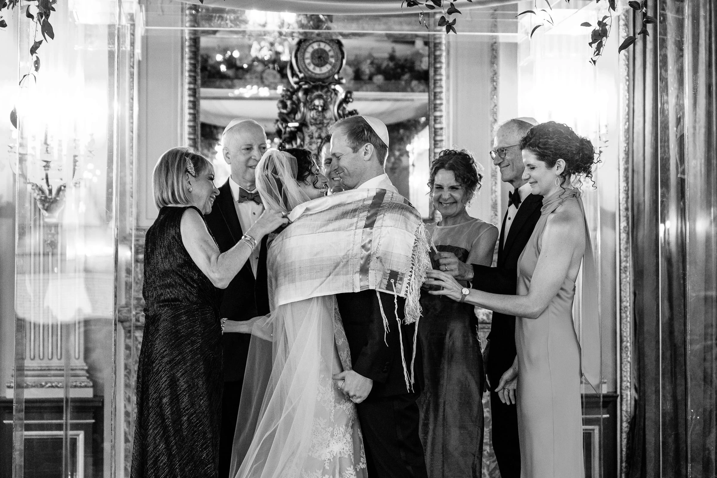 The couple kissing beneath a tallit held up by their parents, in black and white — Metropolitan Club, New York