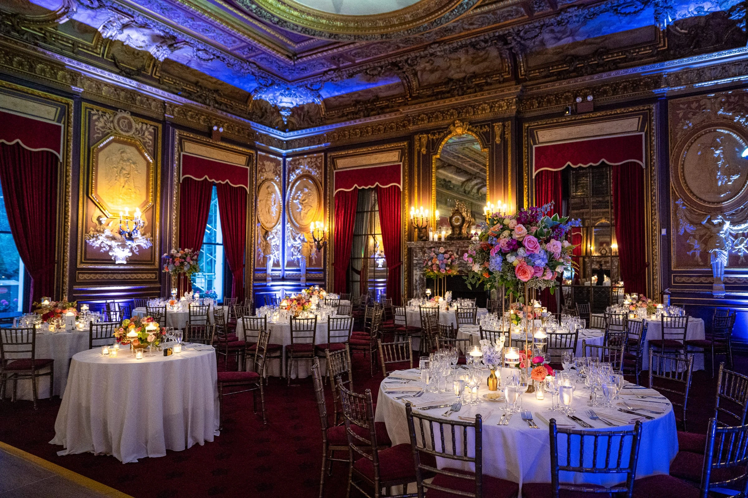 The ballroom set for dinner, candlelit round tables and tall flowers under blue light — Metropolitan Club, New York