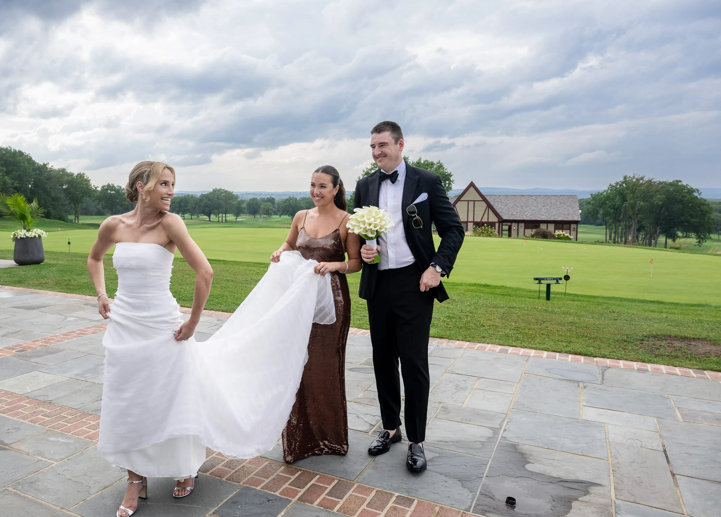 A bridesmaid carrying the bride's train as the couple cross the terrace — Mountain Ridge Country Club, West Caldwell