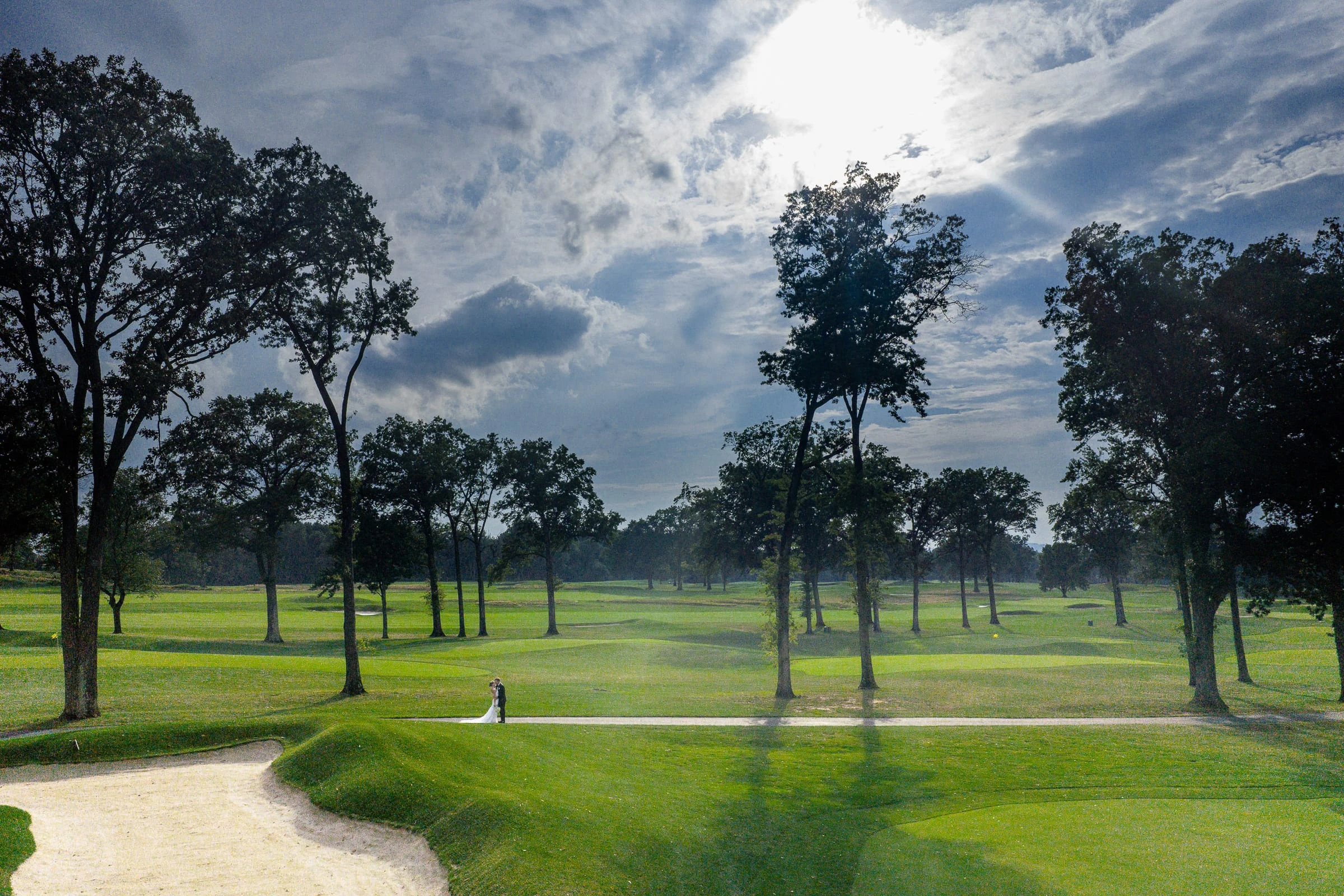 The couple tiny beneath a wide cloud-filled sky on the course — Mountain Ridge Country Club, West Caldwell