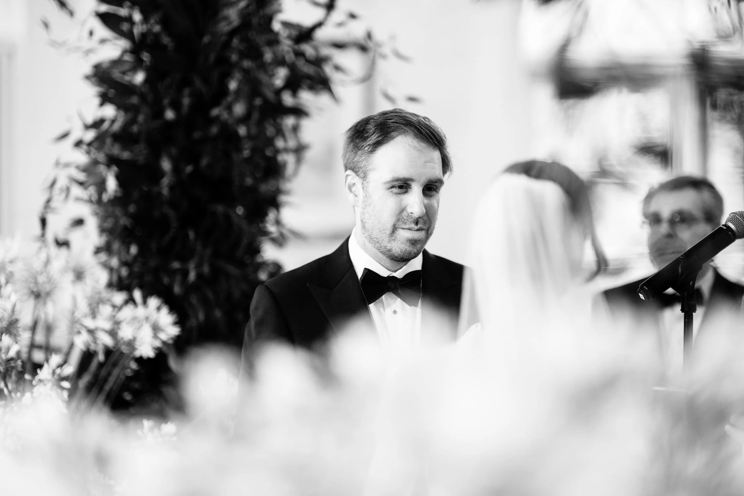 The groom smiling across at the bride during the ceremony, in black and white — Mountain Ridge Country Club, West Caldwell