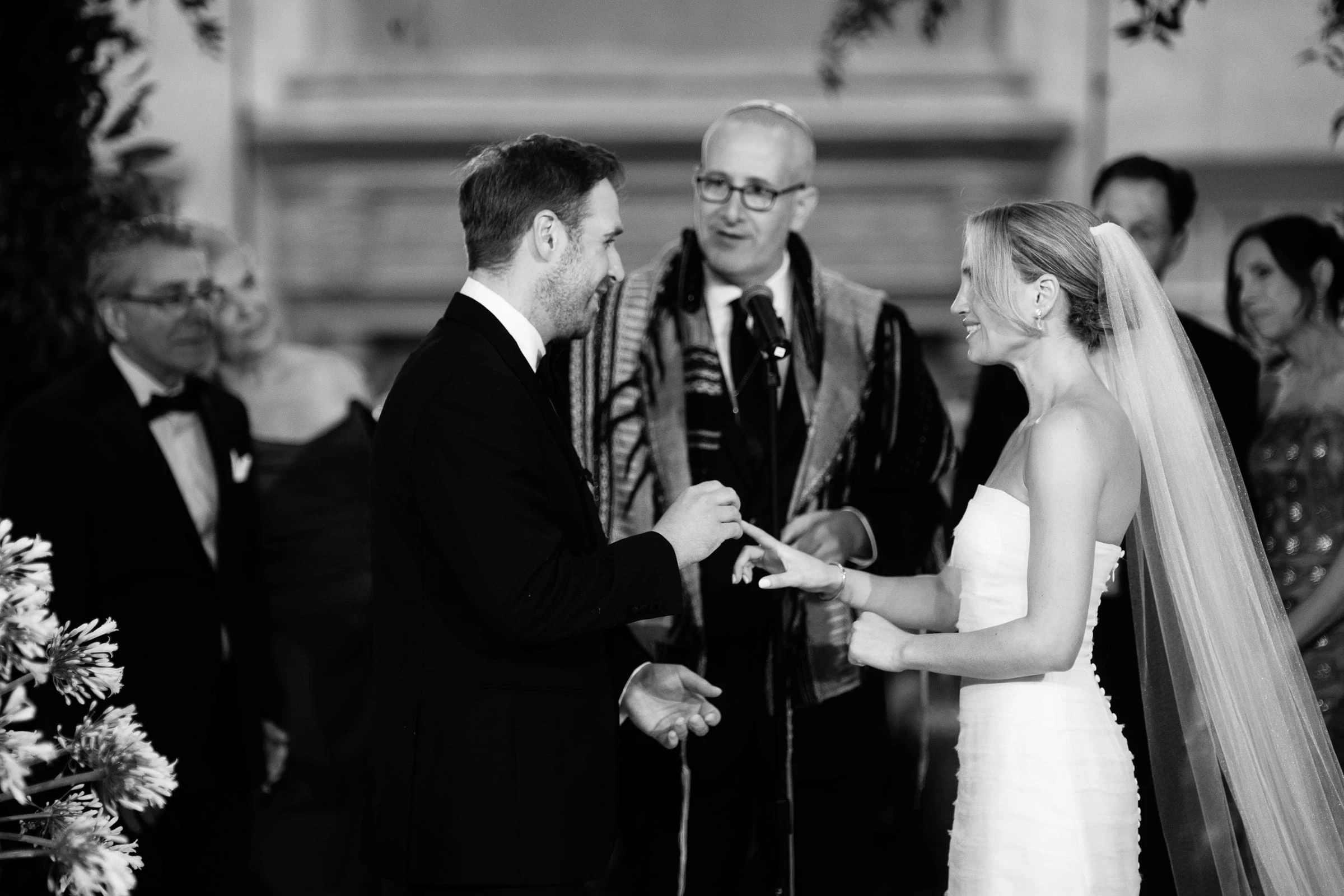 The groom placing the ring on the bride's finger beside the officiant, in black and white — Mountain Ridge Country Club, West Caldwell