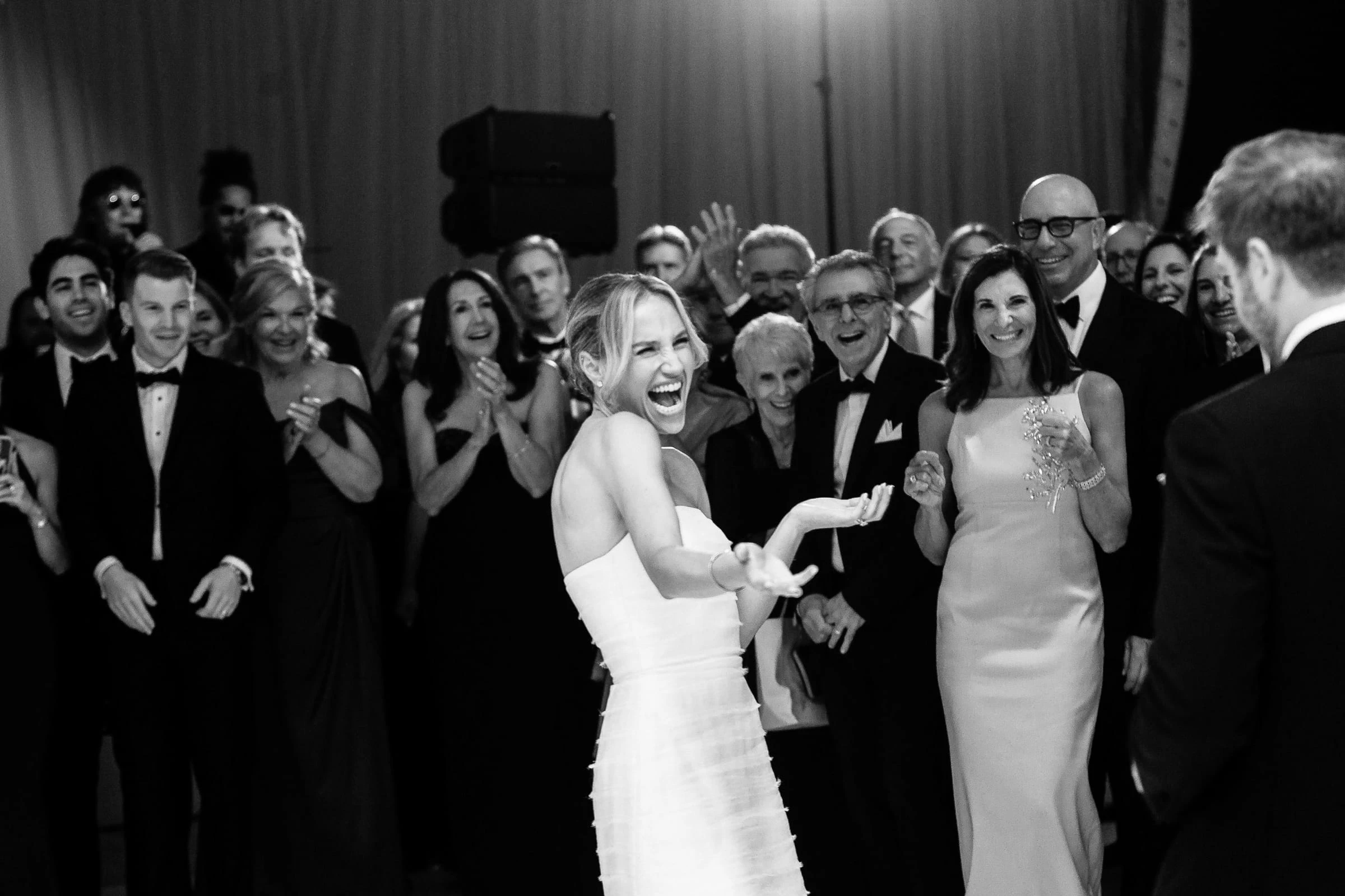 The bride laughing among cheering guests on the dance floor, in black and white — Mountain Ridge Country Club, West Caldwell