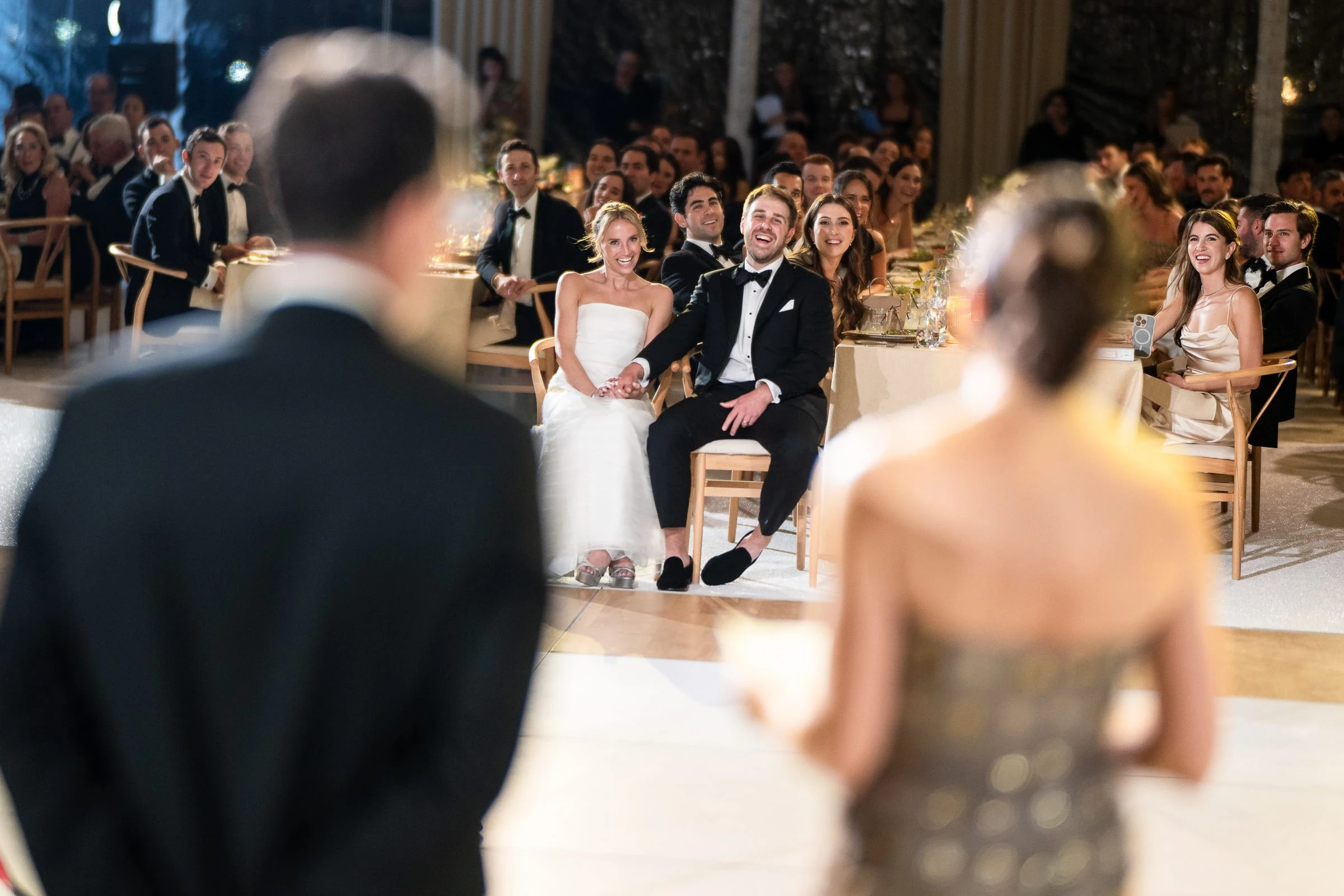 The couple watching the toasts from their seats, seen past two guests in the foreground — Mountain Ridge Country Club, West Caldwell