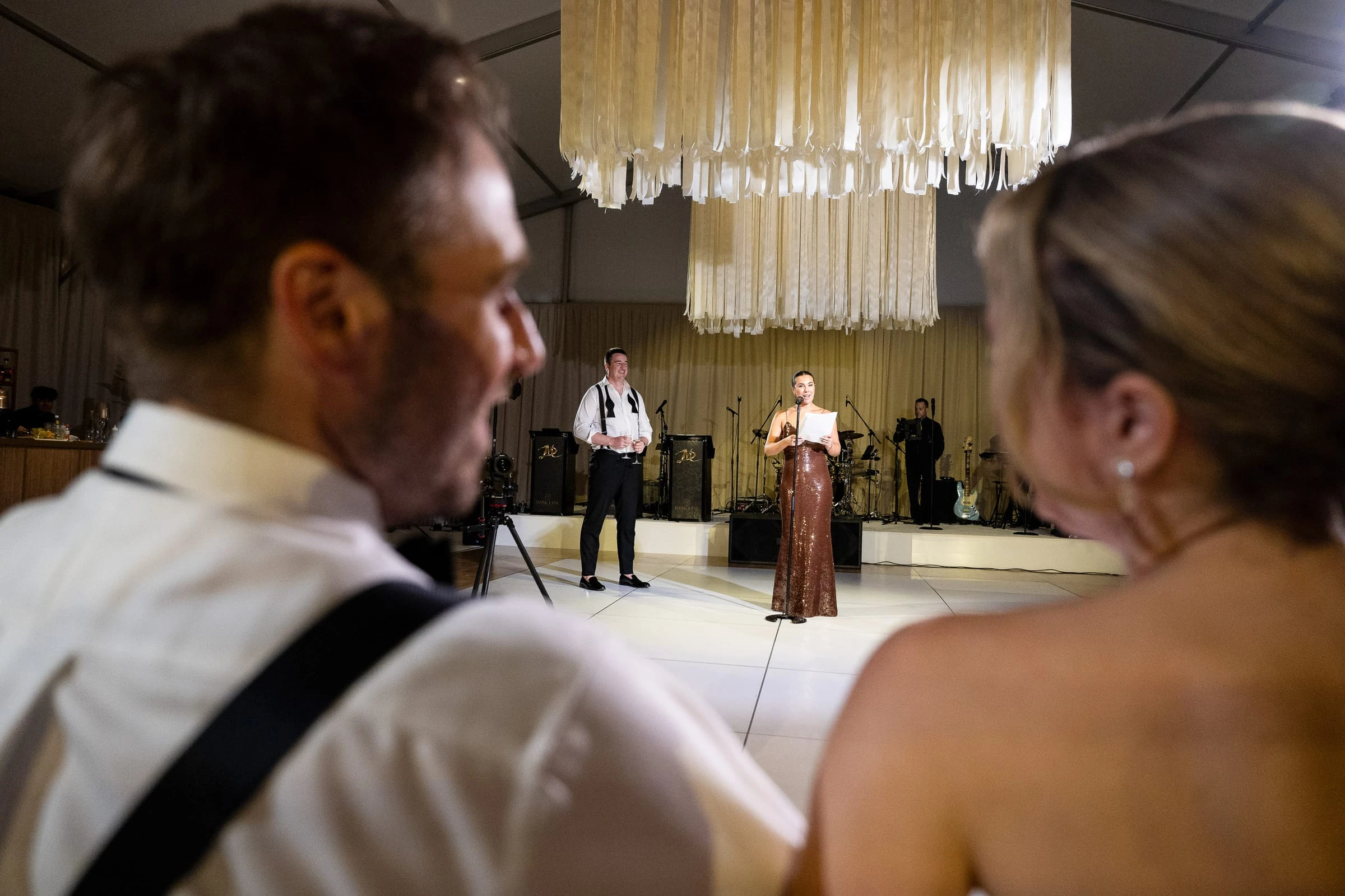 A singer performing on the dance floor beneath the hanging chandelier, seen past two guests — Mountain Ridge Country Club, West Caldwell
