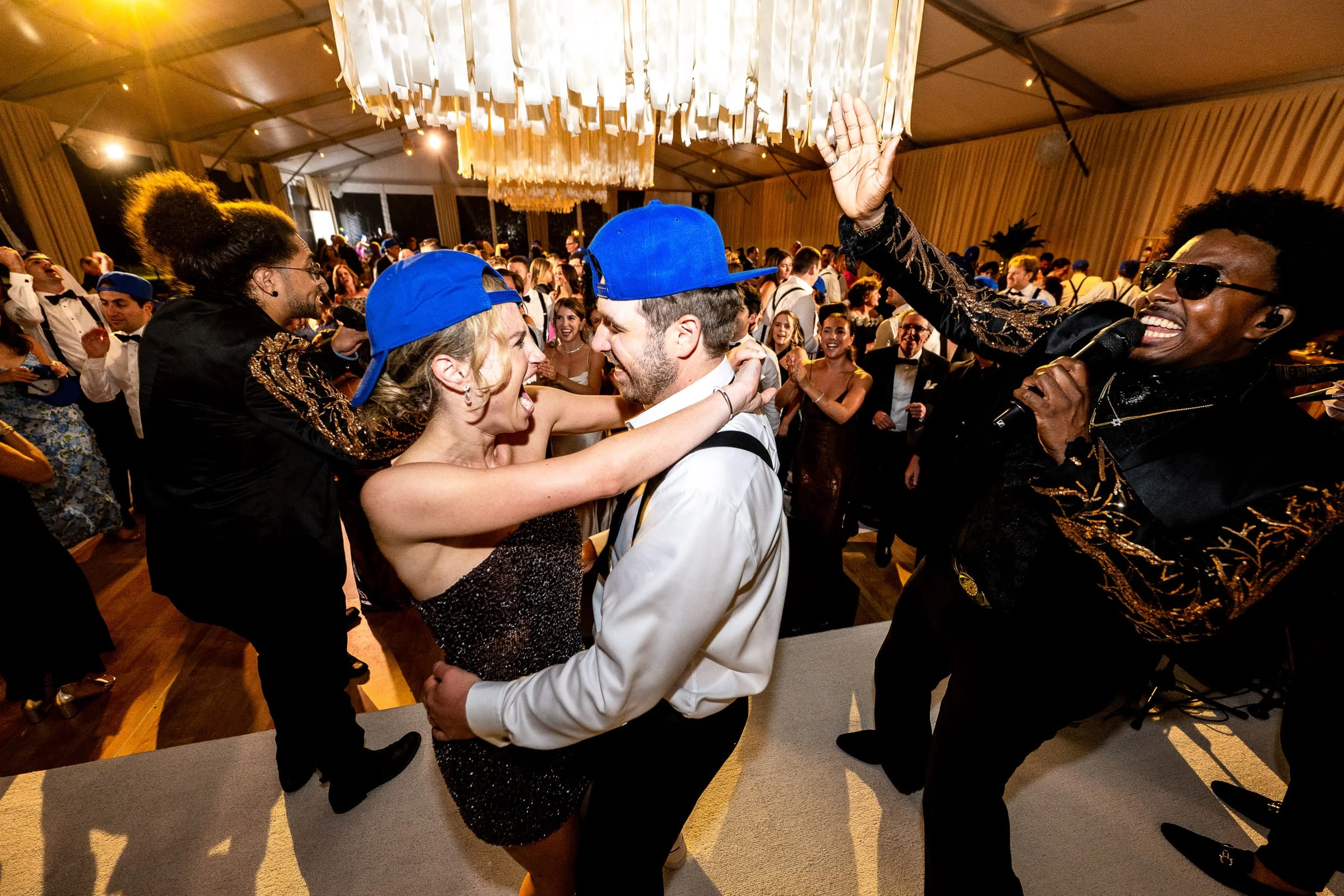 The bride and groom in matching blue caps dancing in a cheering crowd — Mountain Ridge Country Club, West Caldwell
