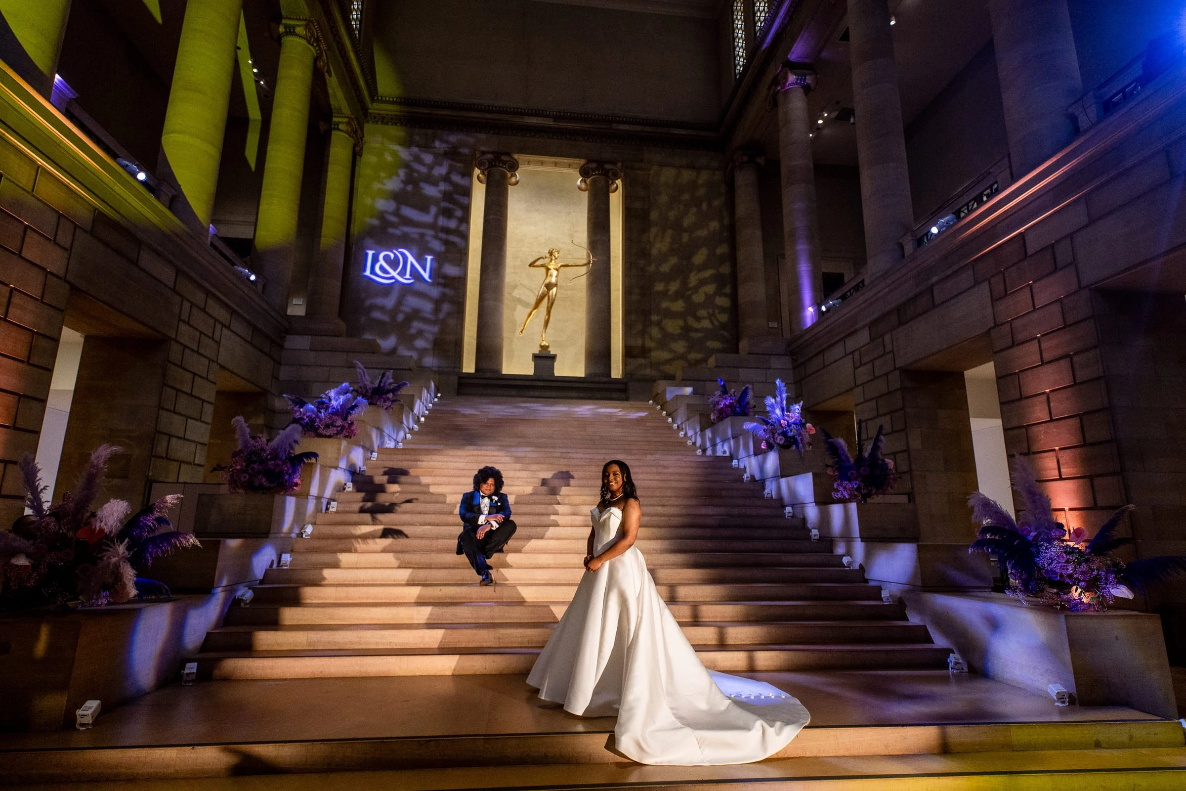 The couple on the grand staircase lit purple beneath the projected monogram — Philadelphia Museum of Art, Philadelphia