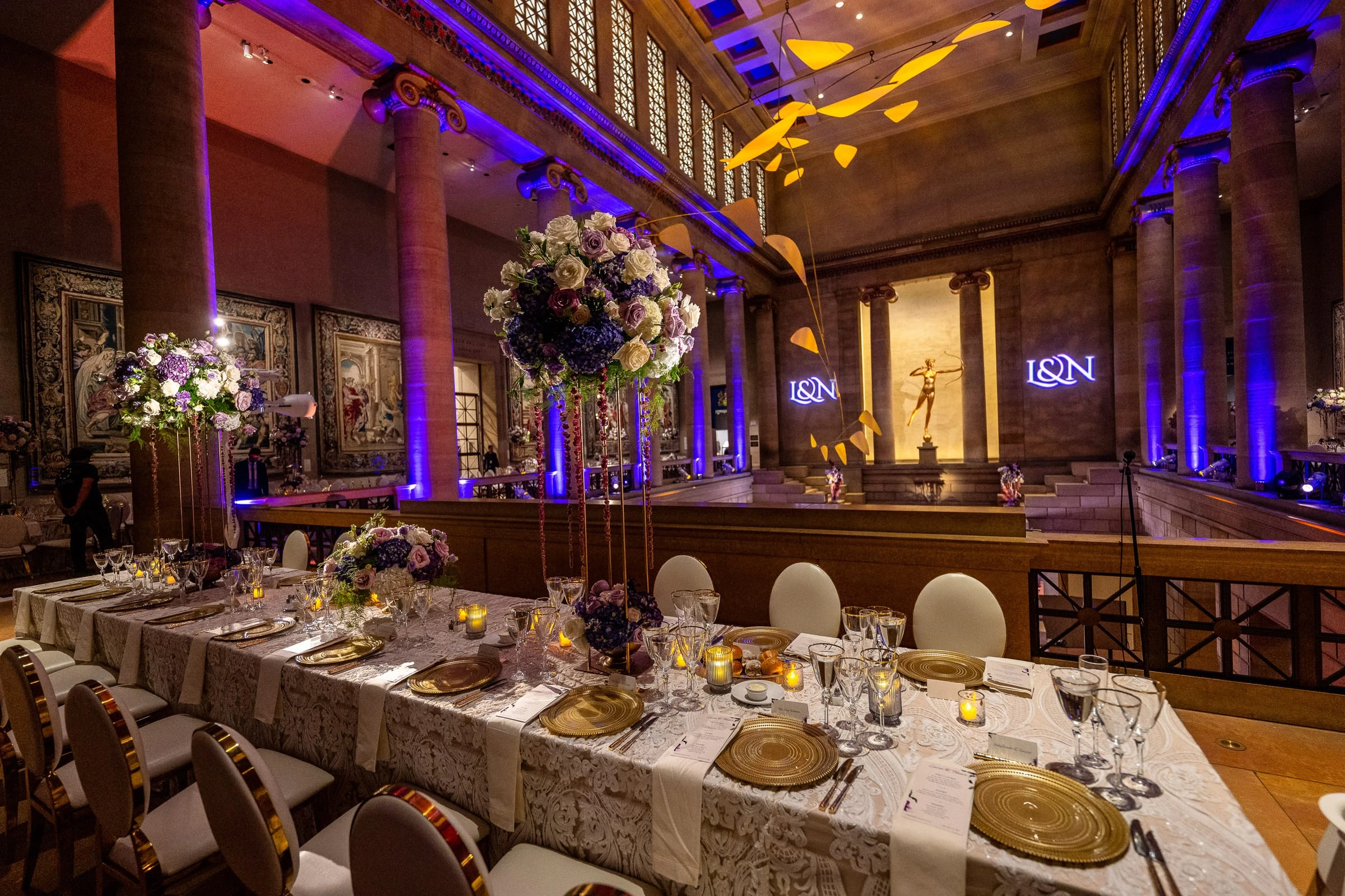 A long banquet table set with gold chargers under blue light — Philadelphia Museum of Art, Philadelphia