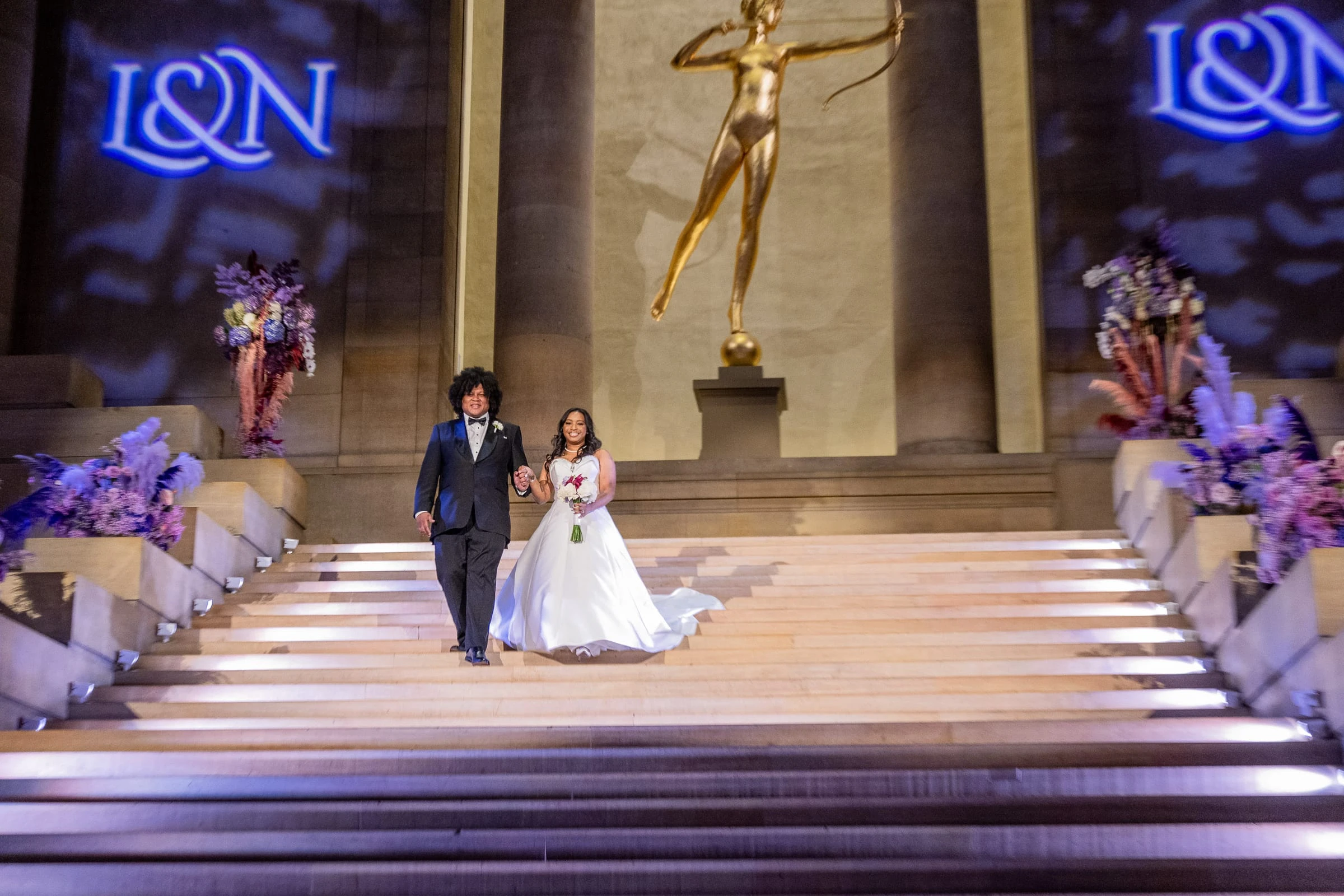 The couple coming down the lit staircase beneath the gilded statue — Philadelphia Museum of Art, Philadelphia