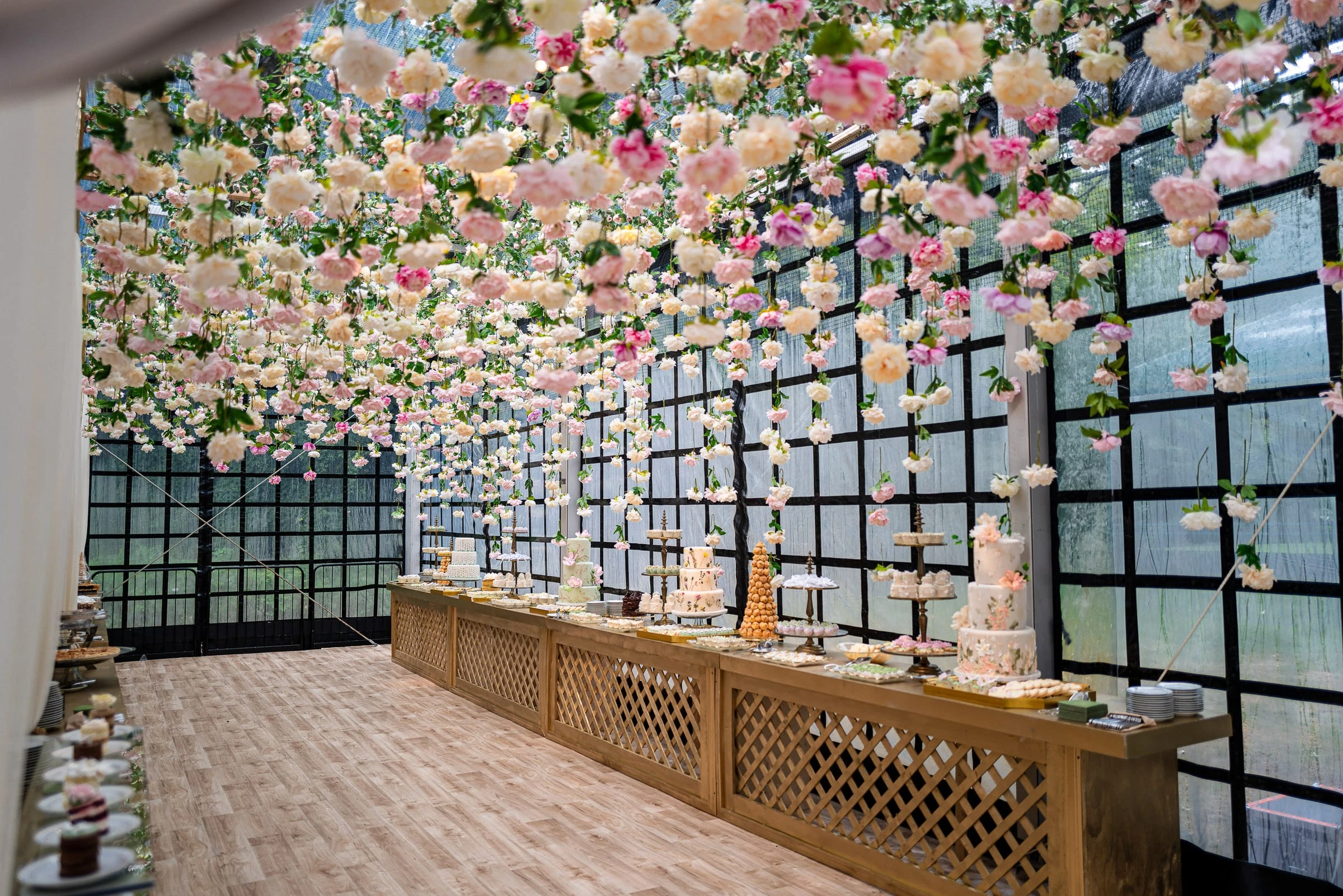 A ceiling of suspended pink and cream roses above a long dessert bar of tiered cakes