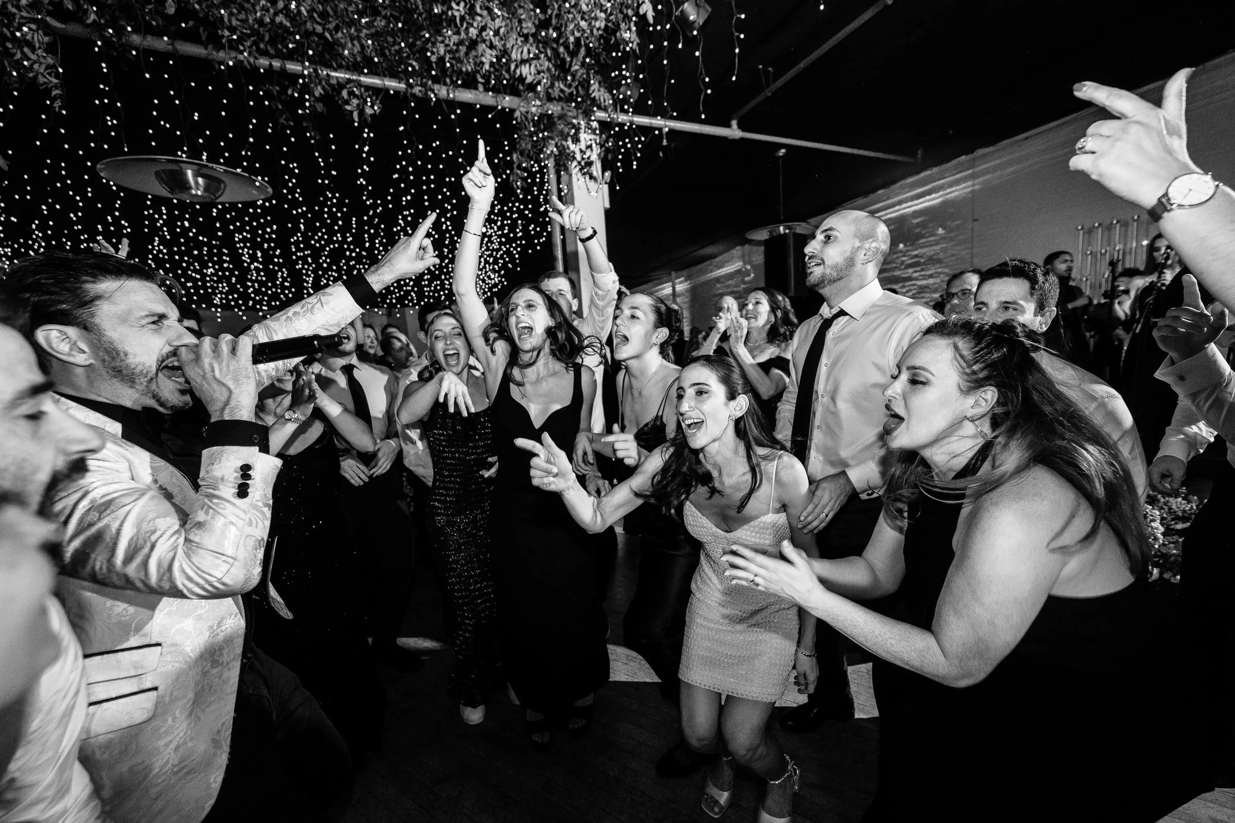 Guests singing and cheering together on the dance floor, in black and white