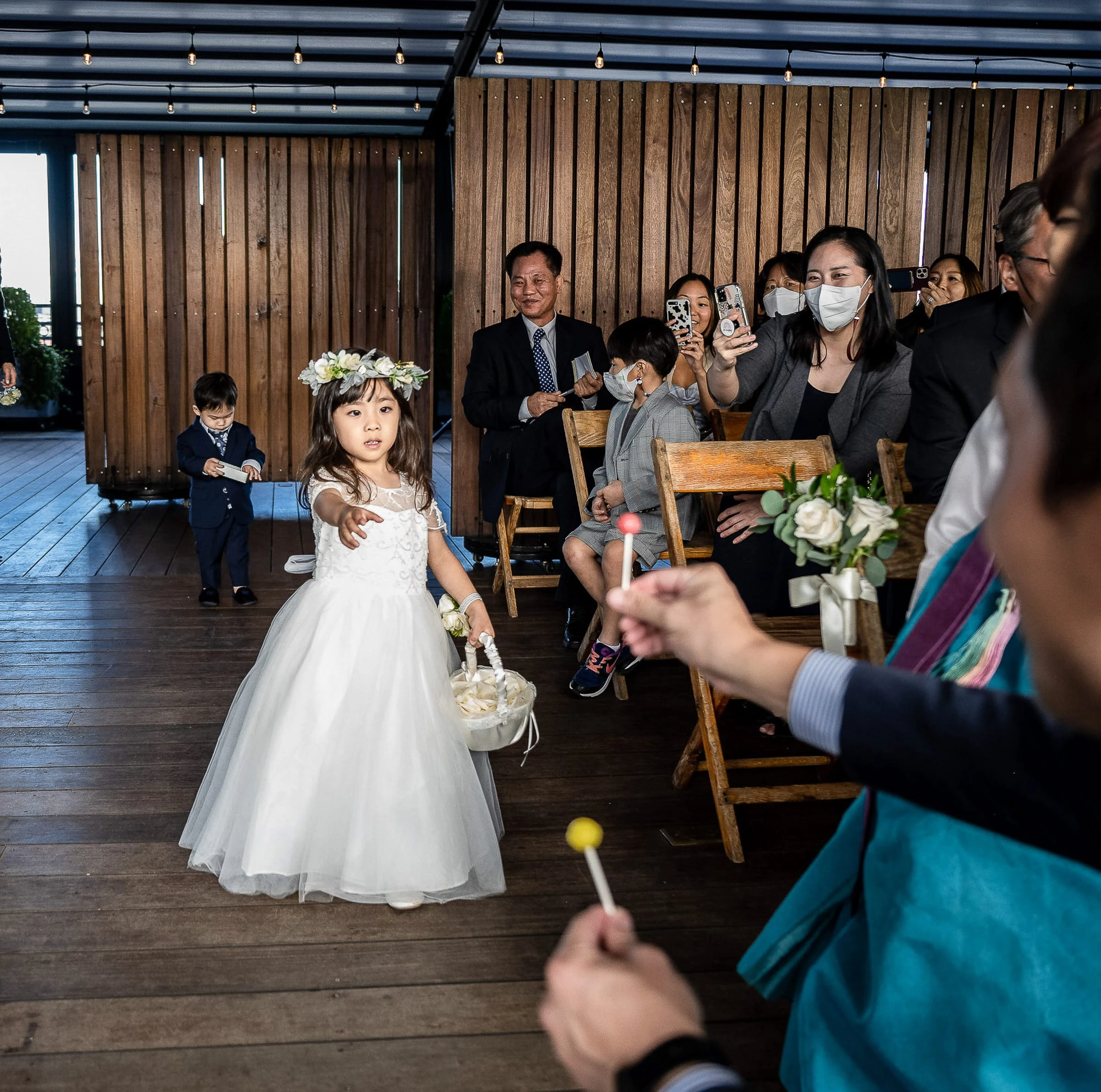 A flower girl walking the aisle with a basket as seated guests watch