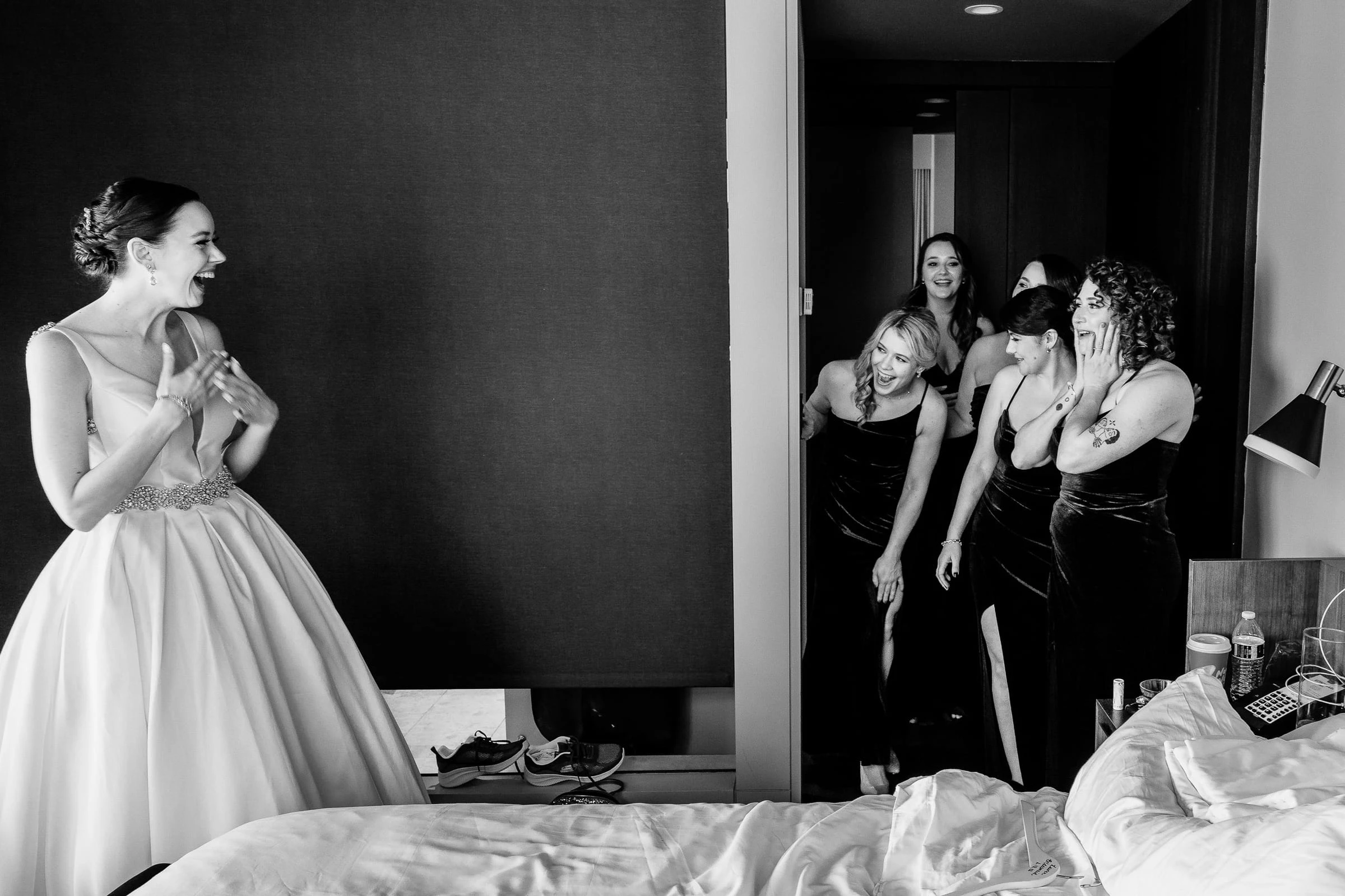 A bride laughing with her bridesmaids in the room before the ceremony, in black and white