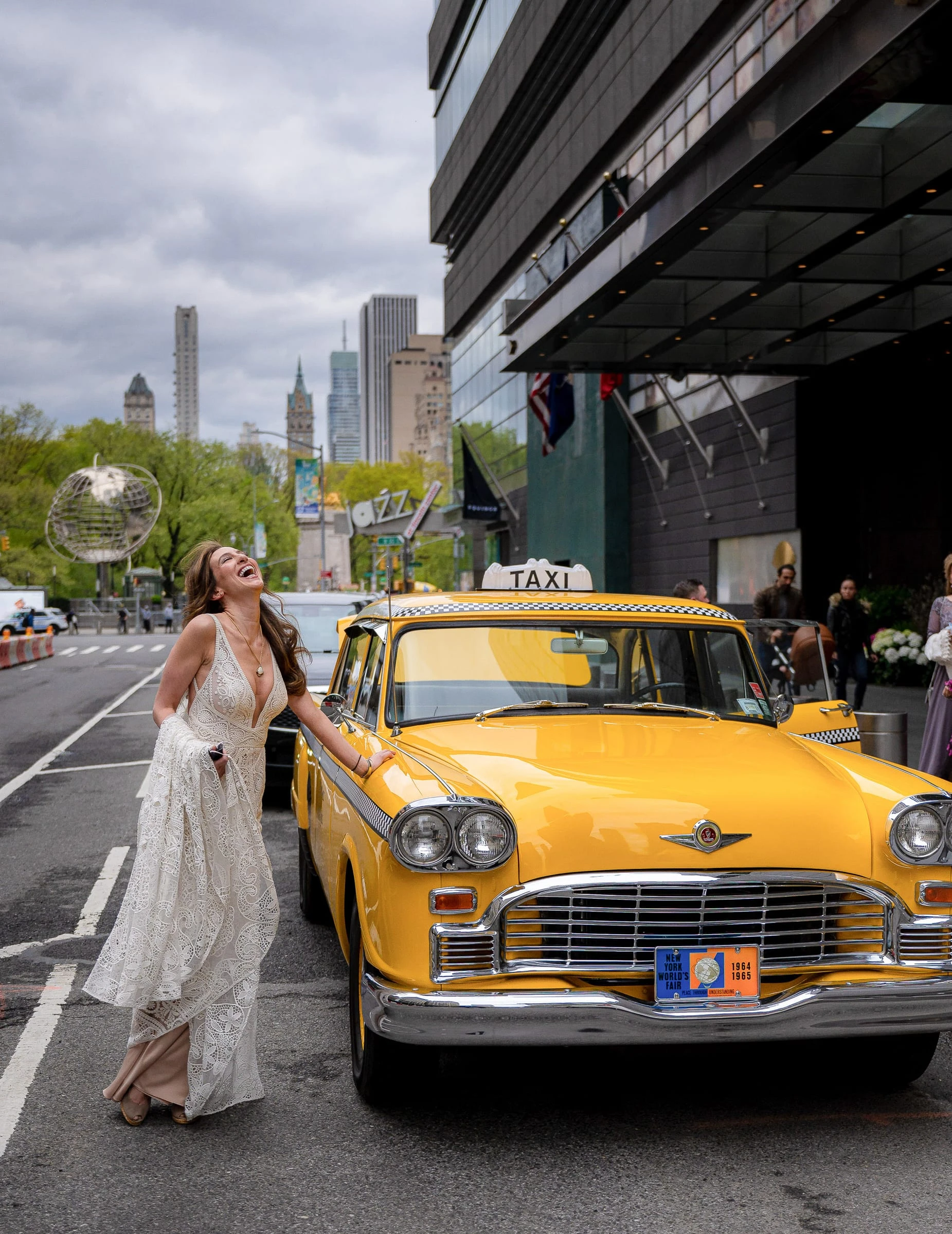 A bride laughing beside a yellow checker taxi on a city street