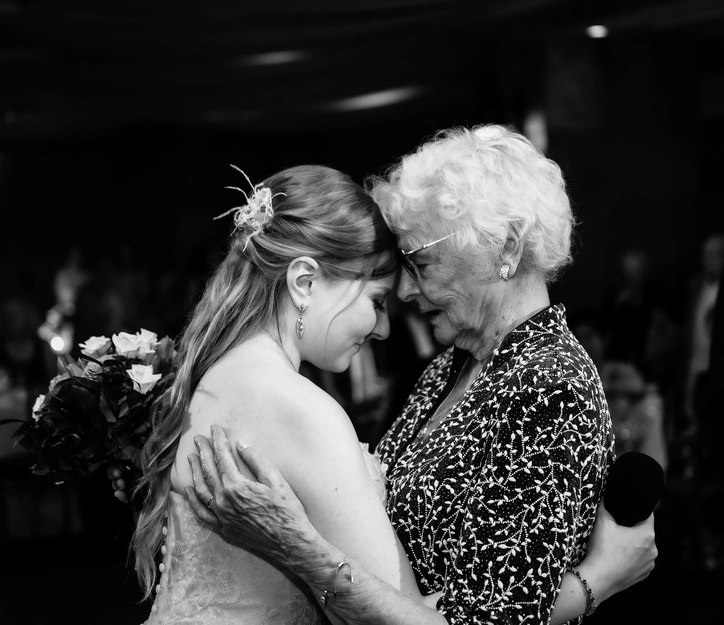A bride dancing cheek to cheek with her grandmother, in black and white