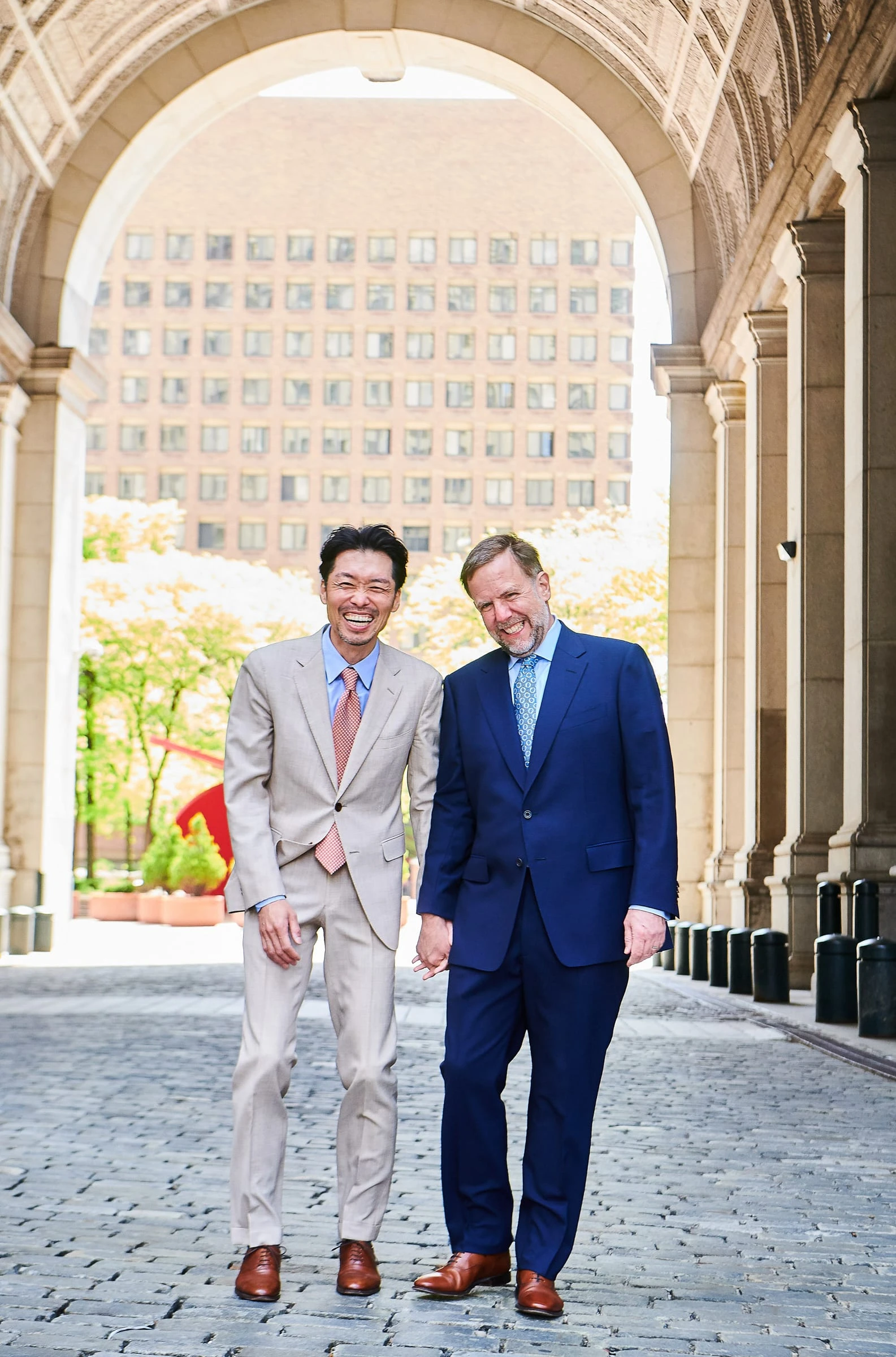 Two grooms smiling together beneath a stone archway