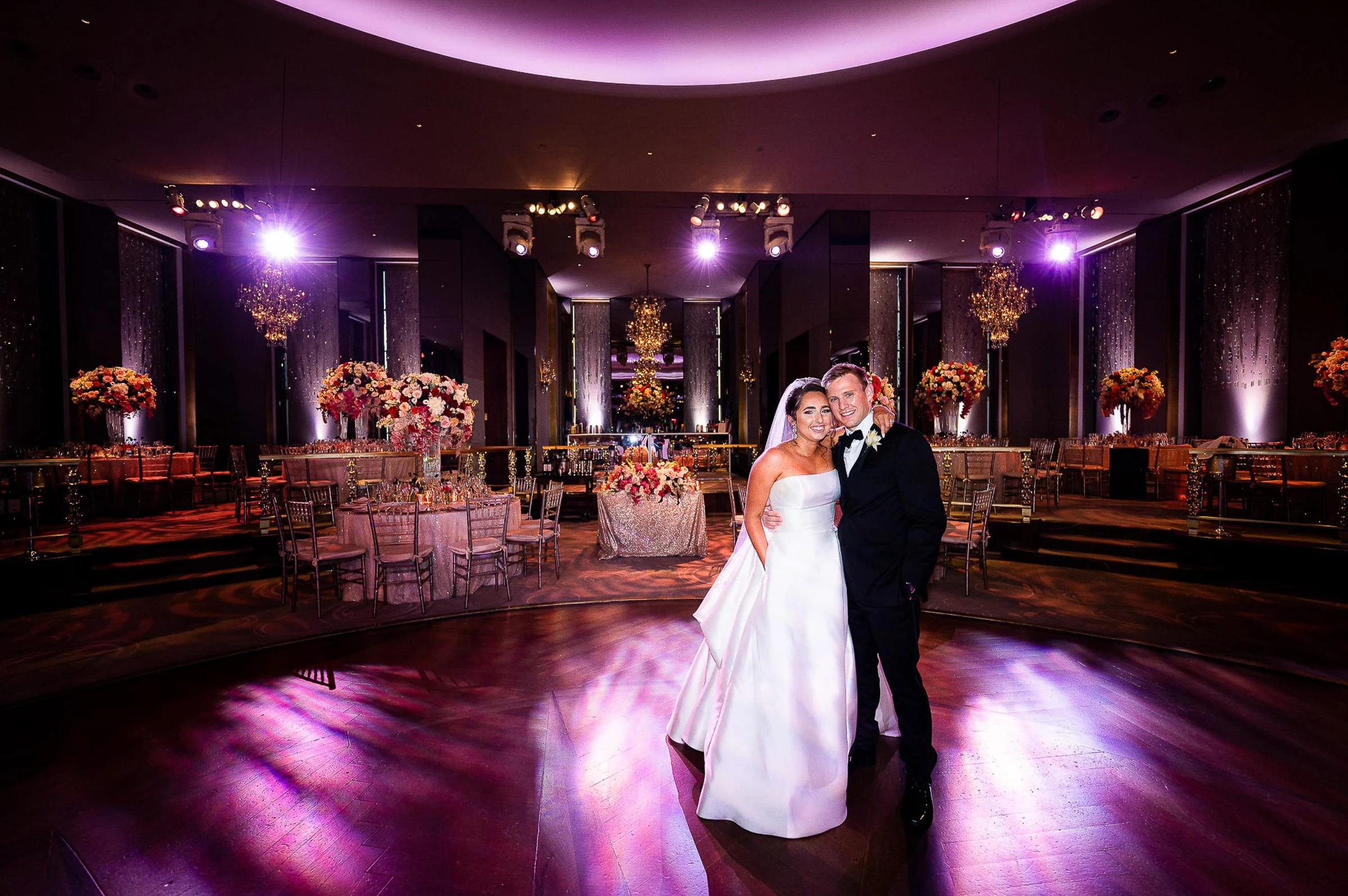 A couple alone on the dance floor of a ballroom lit in purple