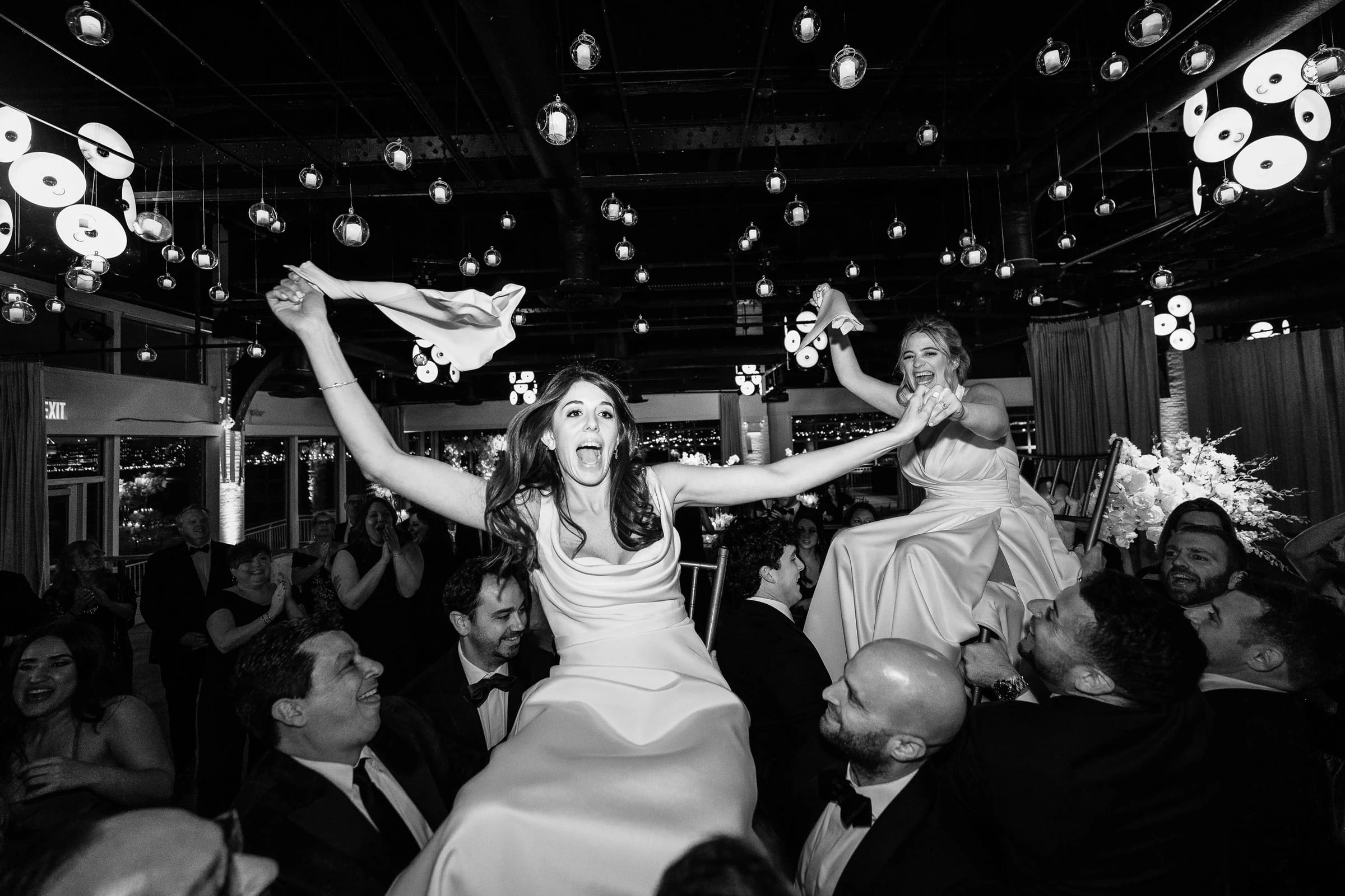 Two women lifted on chairs and waving napkins during the hora, in black and white