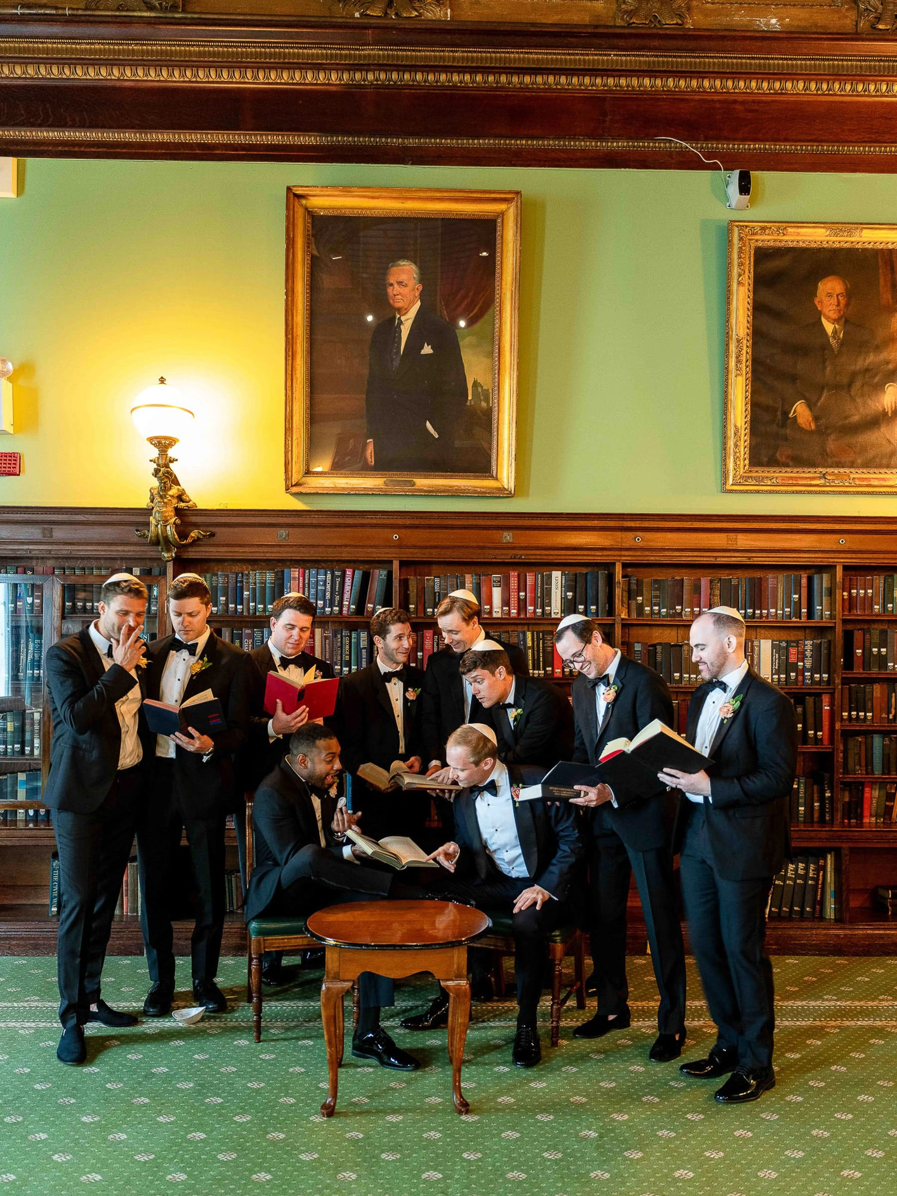 Groomsmen arranged around a table in a wood-panelled library hung with portraits