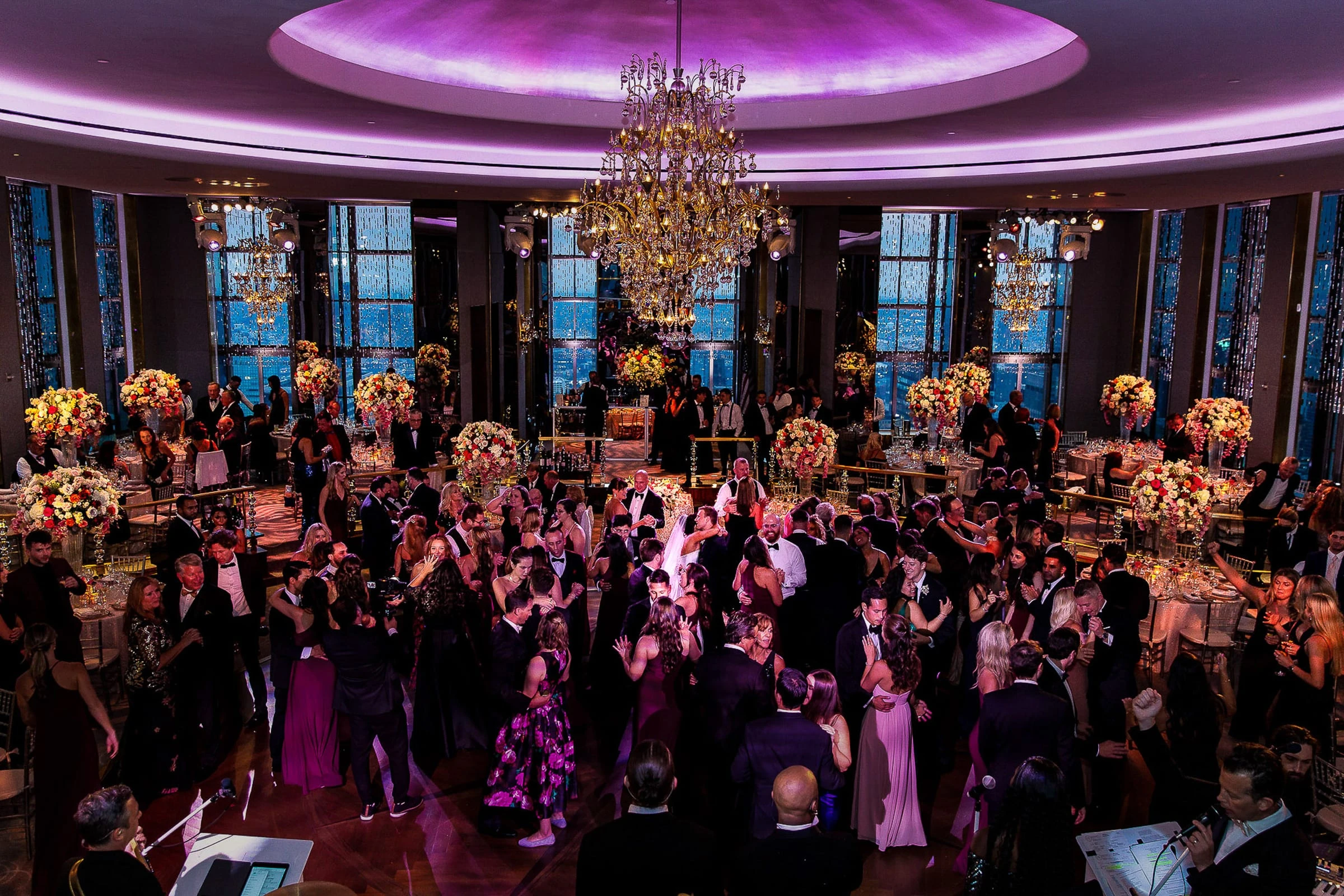 A crowded dance floor beneath a chandelier and a violet-lit dome